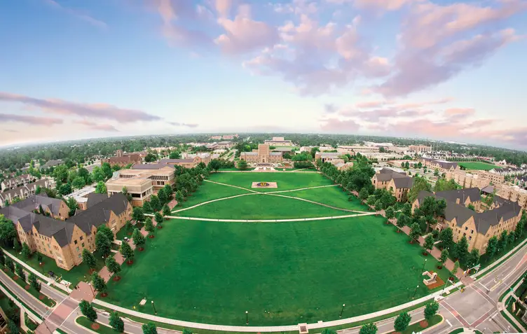 Aerial view of a university campus quadrangle with lawns, intersecting walkways, academic buildings, and a sunset sky.