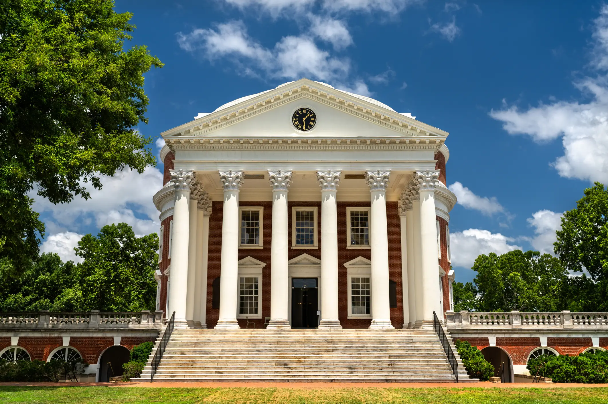 The Rotunda at the University of Virginia stands behind broad steps under a blue, partly cloudy sky.