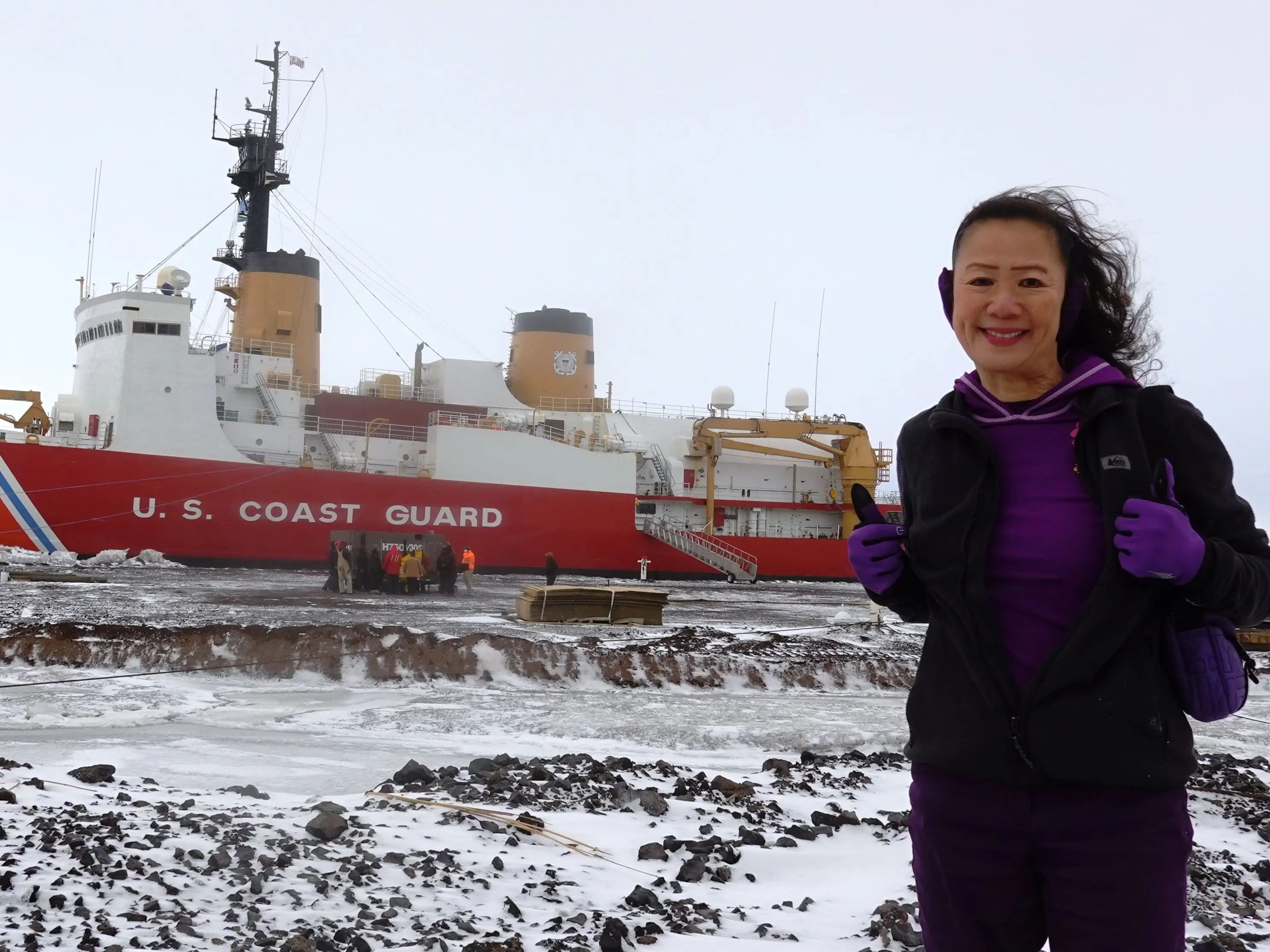 Person stands on a snowy shoreline in front of a red U. S. Coast Guard ship marked 10.