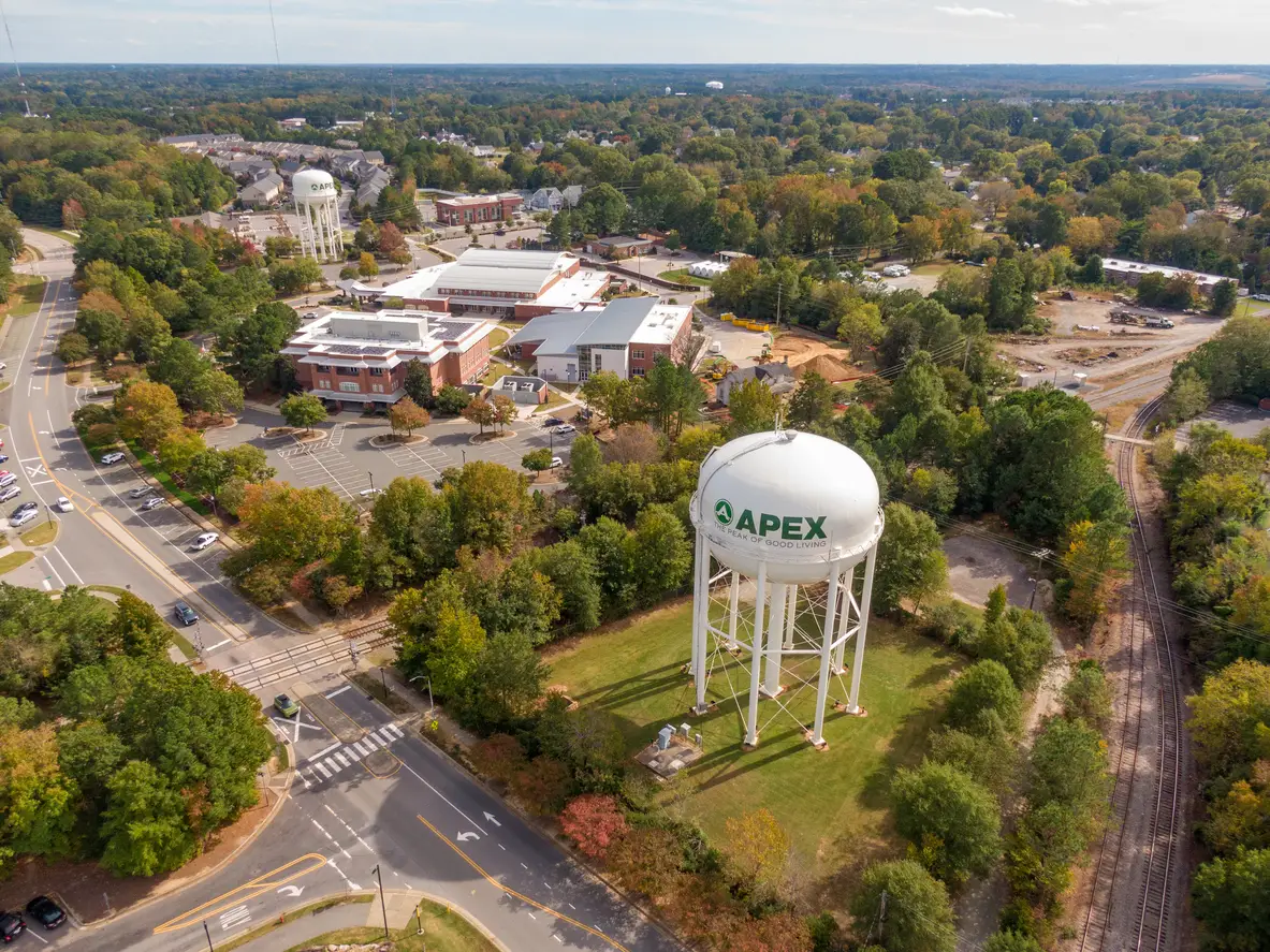 High-angle drone photography on a bright, sunny day capturing key landmarks and the historic downtown area of Apex, North Carolina.