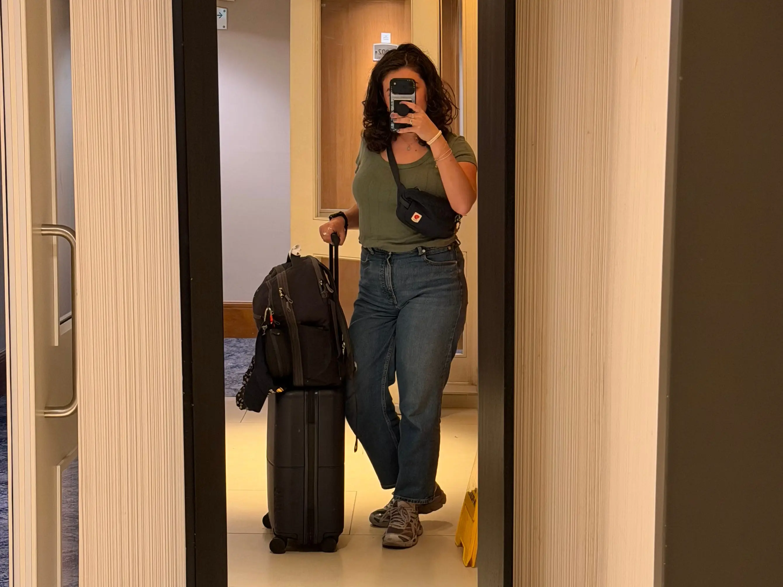 The writer is taking a mirror selfie with her luggage in a hallway.