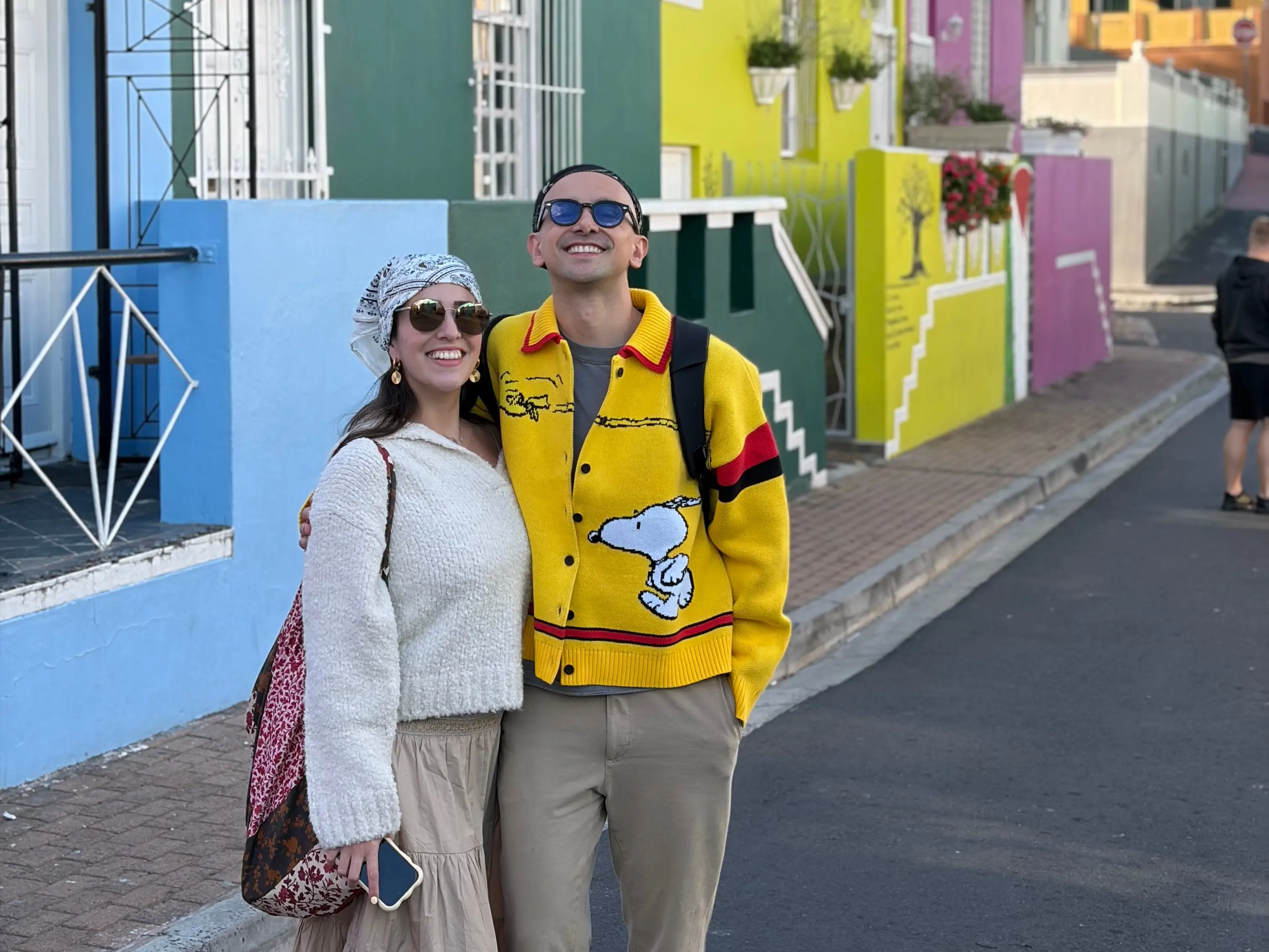 The writer and his partner wear sunglasses and smile for the camera in front of colorful houses.