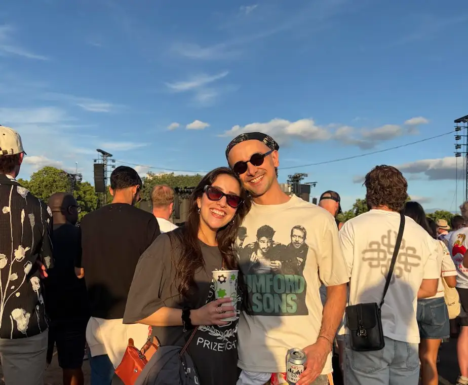 The writer and his partner holding drinks and wearing band shirts while outside at a music festival.