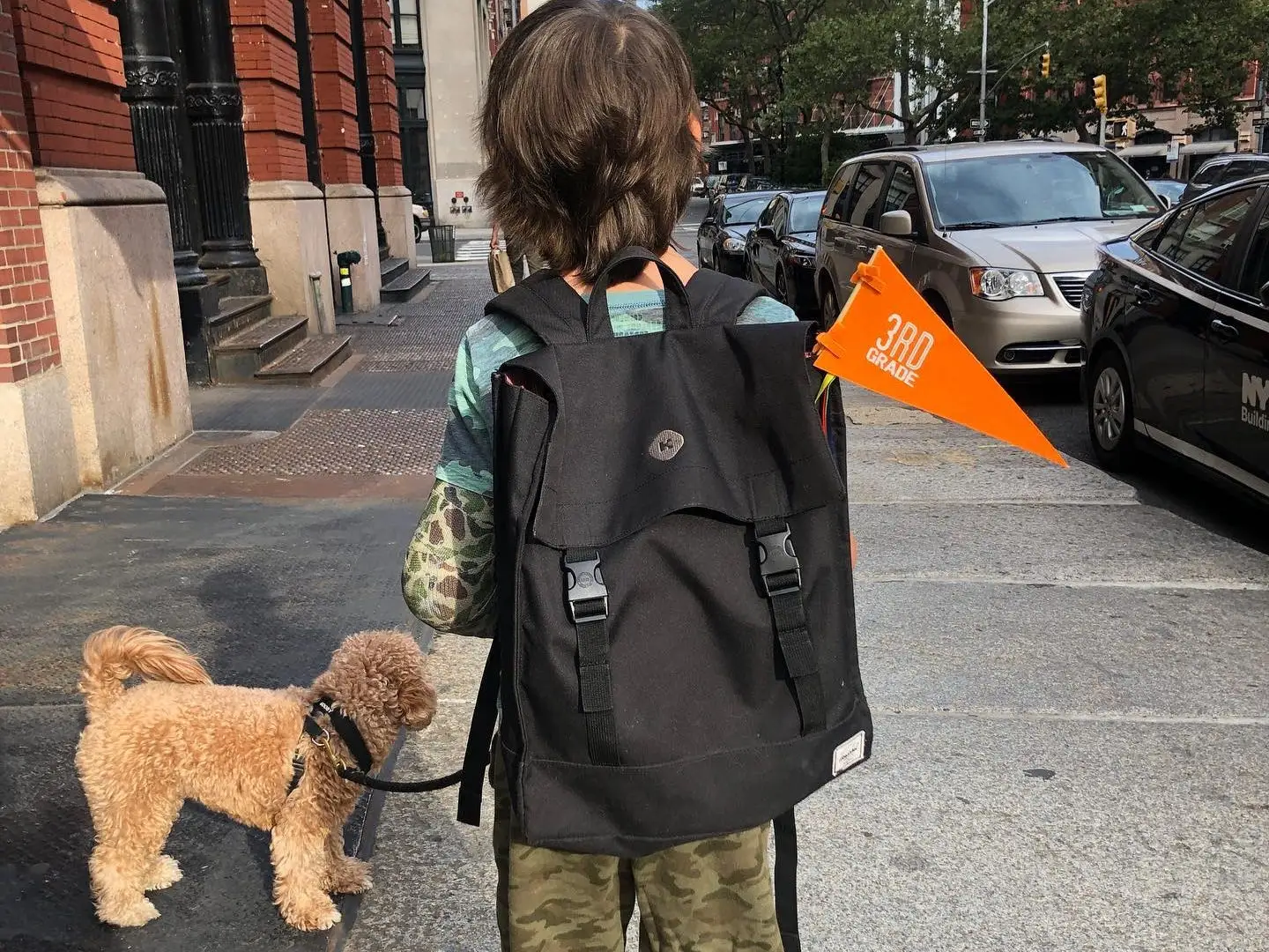 Kid with backpack walking in NYC with dog nearby