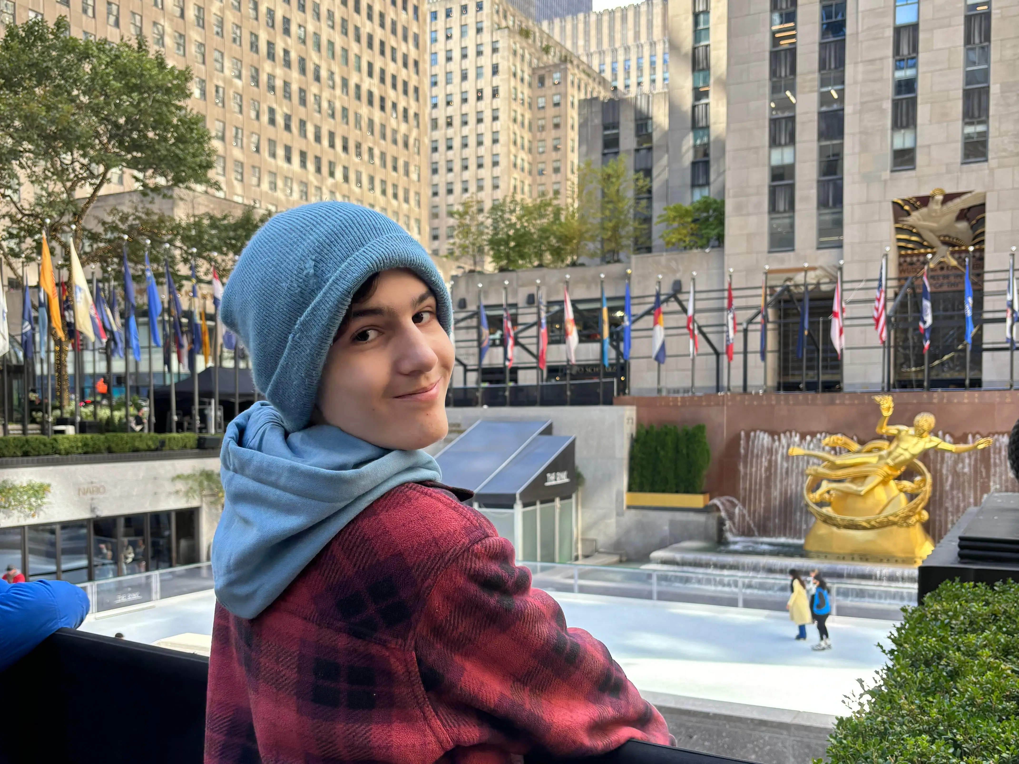 Visitor in blue hood and red plaid jacket overlooks the Rockefeller Center ice rink and Prometheus statue.