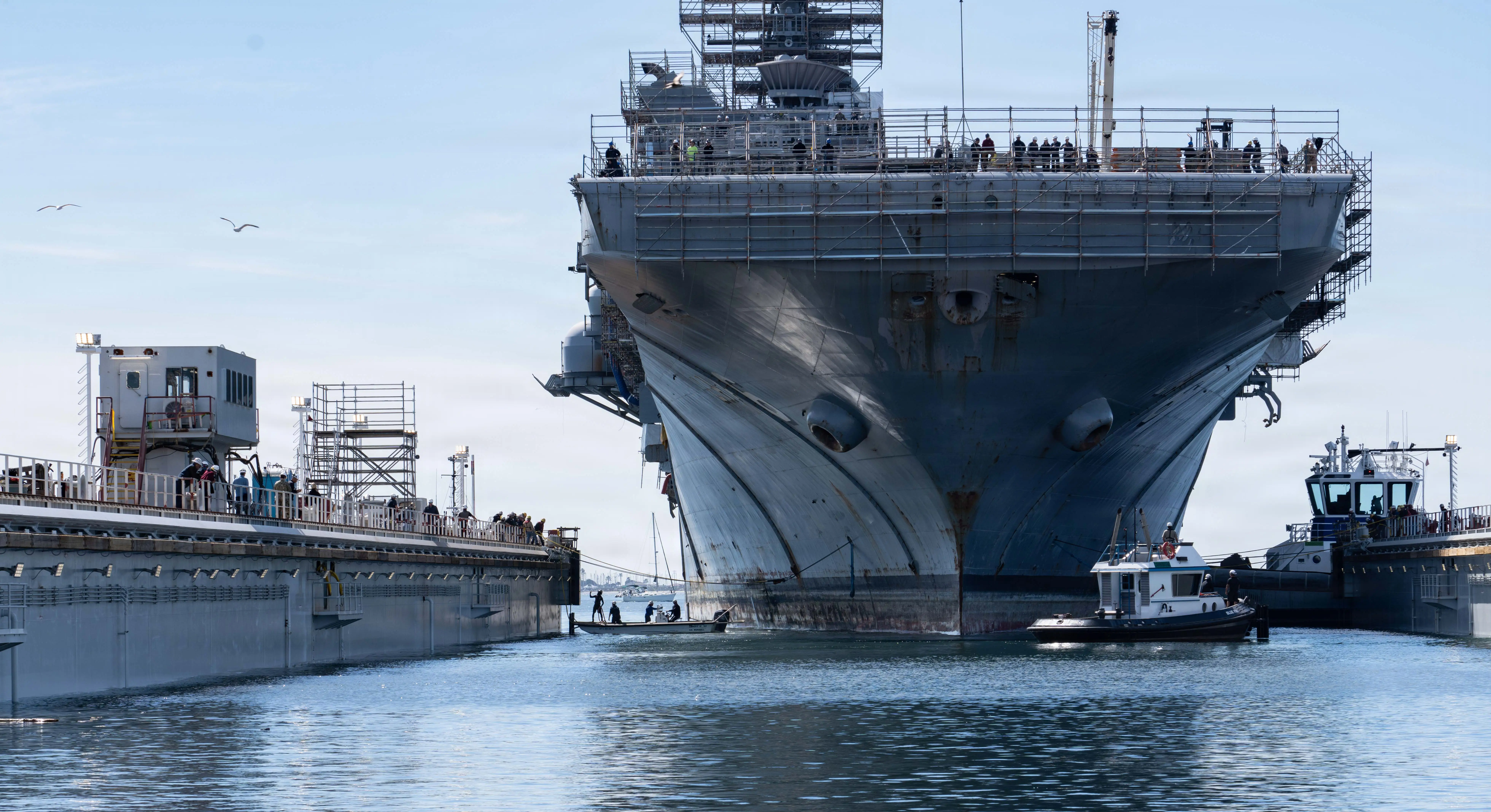 An amphibious assault ship pulls into a shipyard's dry dock.