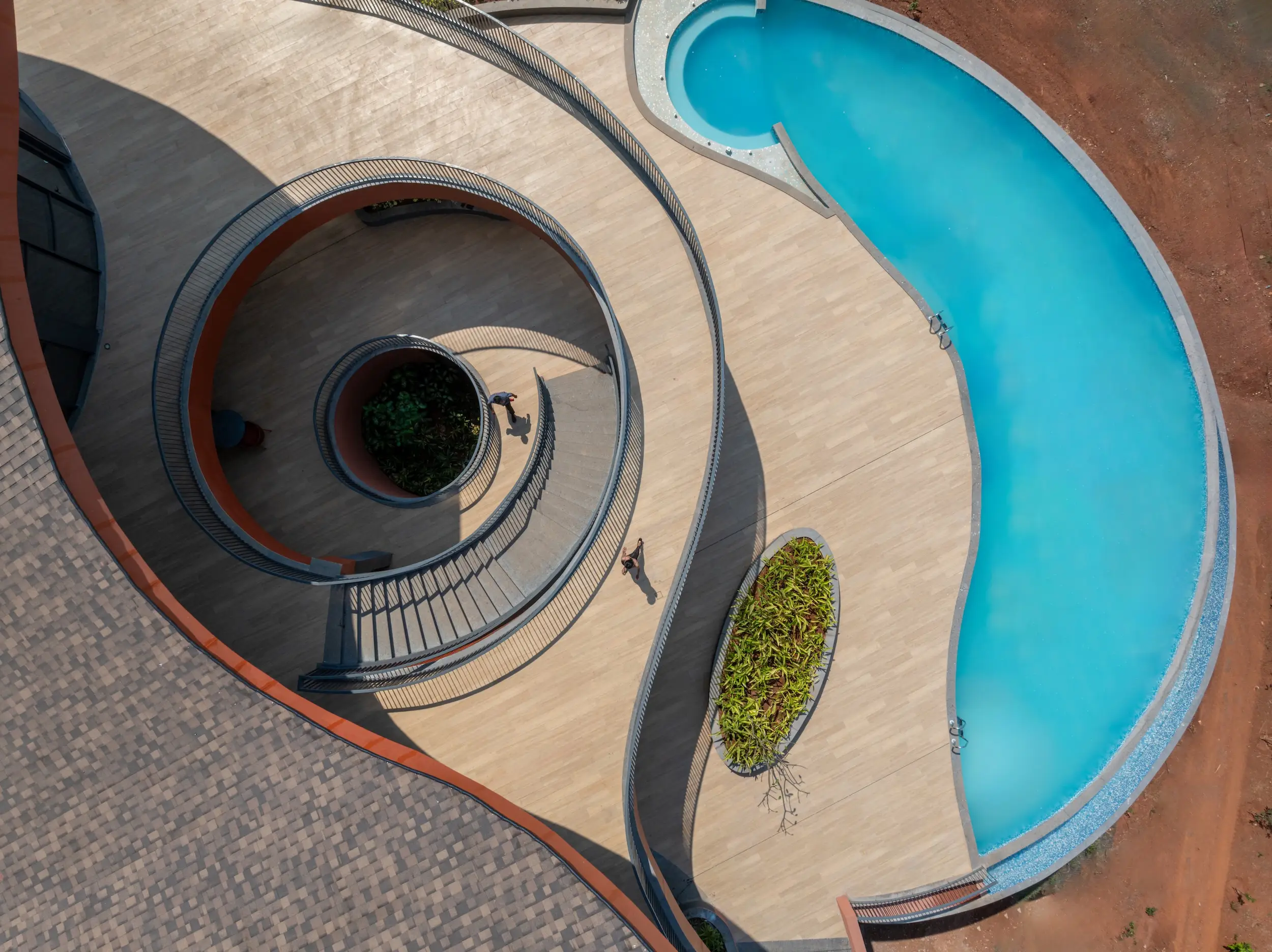 Aerial view of a spiral walkway beside a curved blue swimming pool with small figures on the deck.