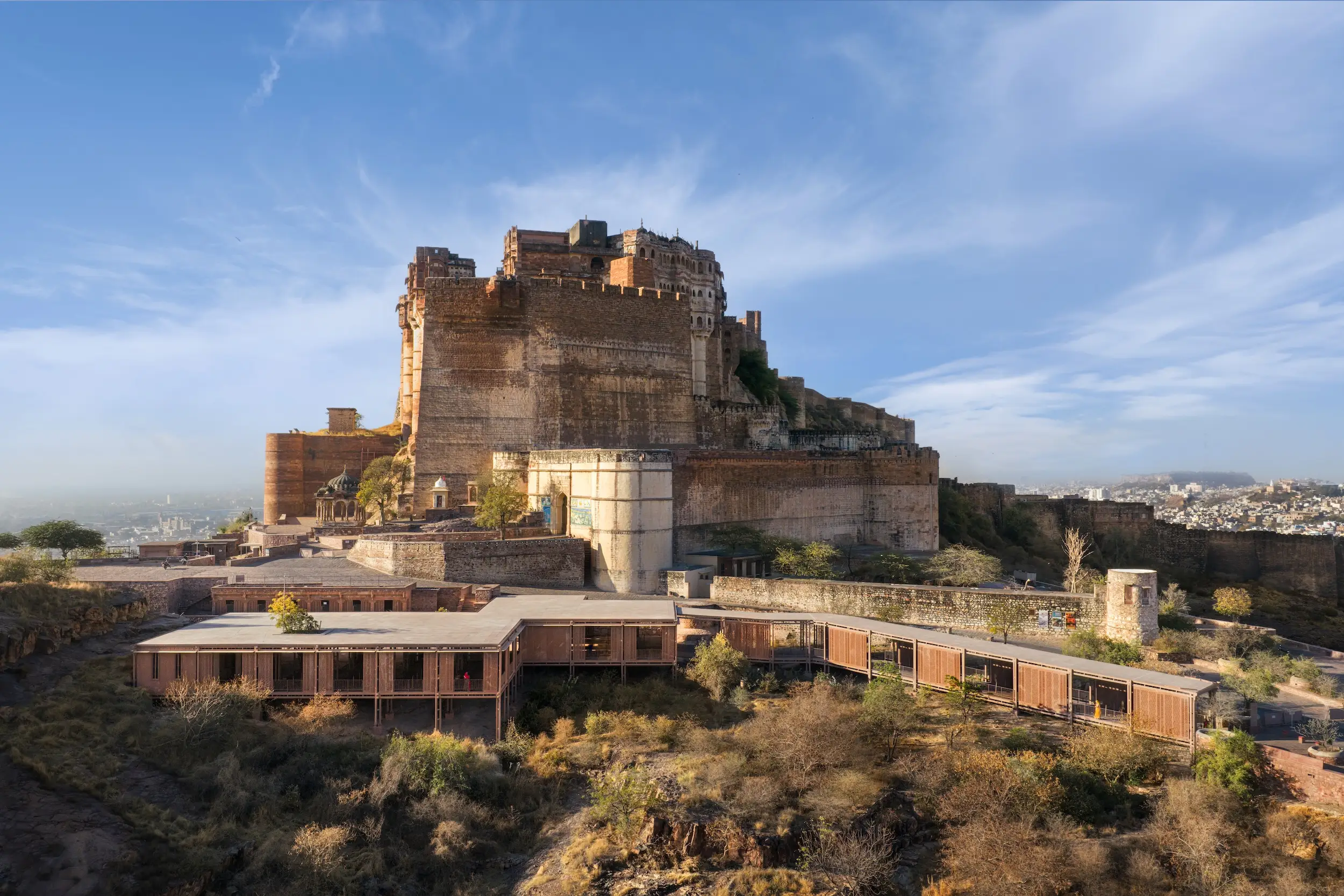 Mehrangarh Fort rises above dry hillside vegetation and city buildings under a blue sky in Jodhpur.