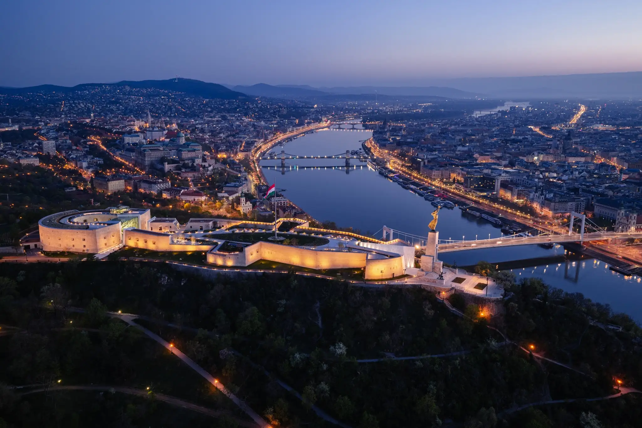 Budapest at dusk with the Danube, Elisabeth Bridge, Citadella, and Liberty Statue illuminated above the city.