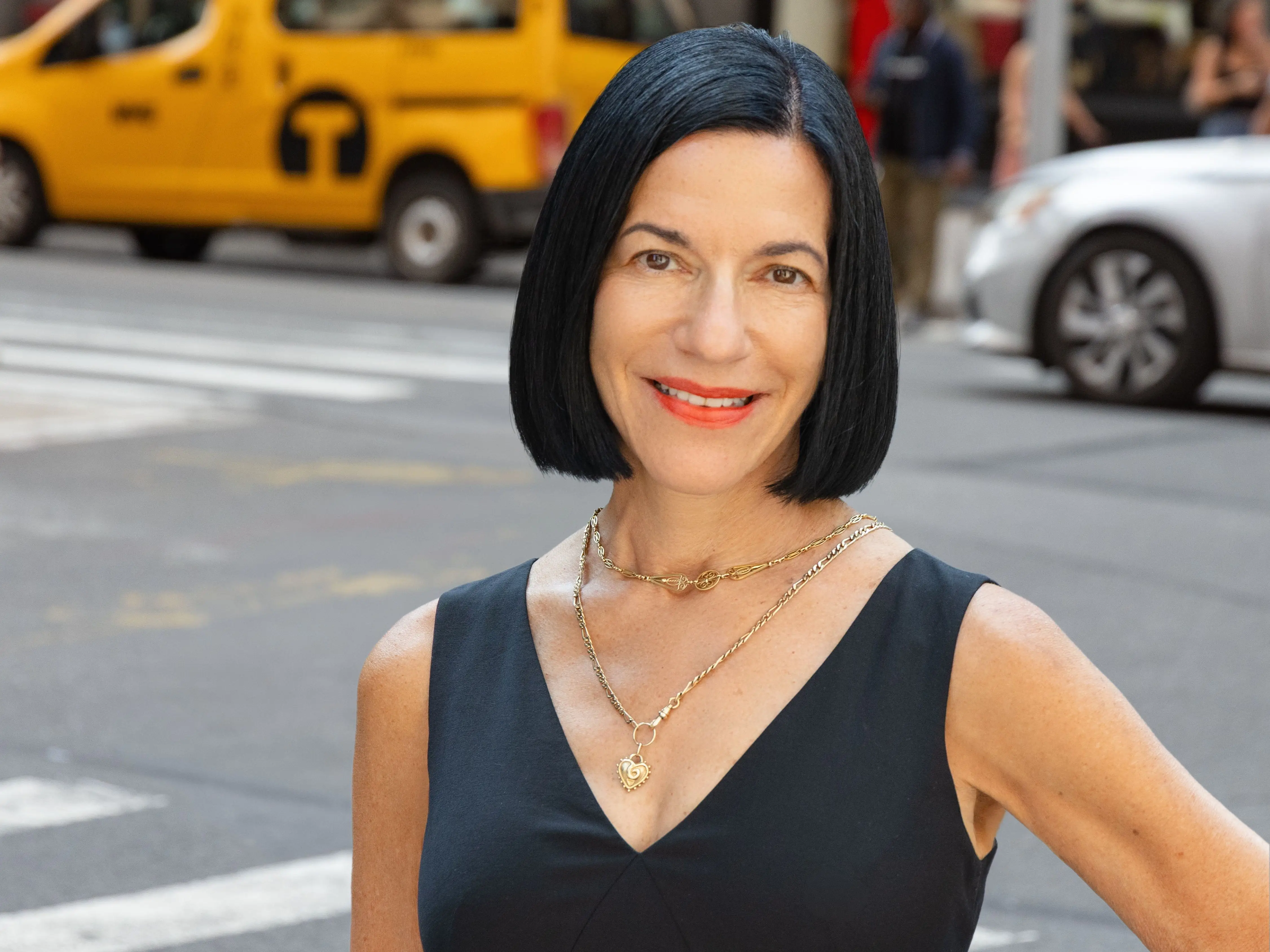 Brigitte Weil on a street in New York with a taxi behind her, she is wearing a black top.