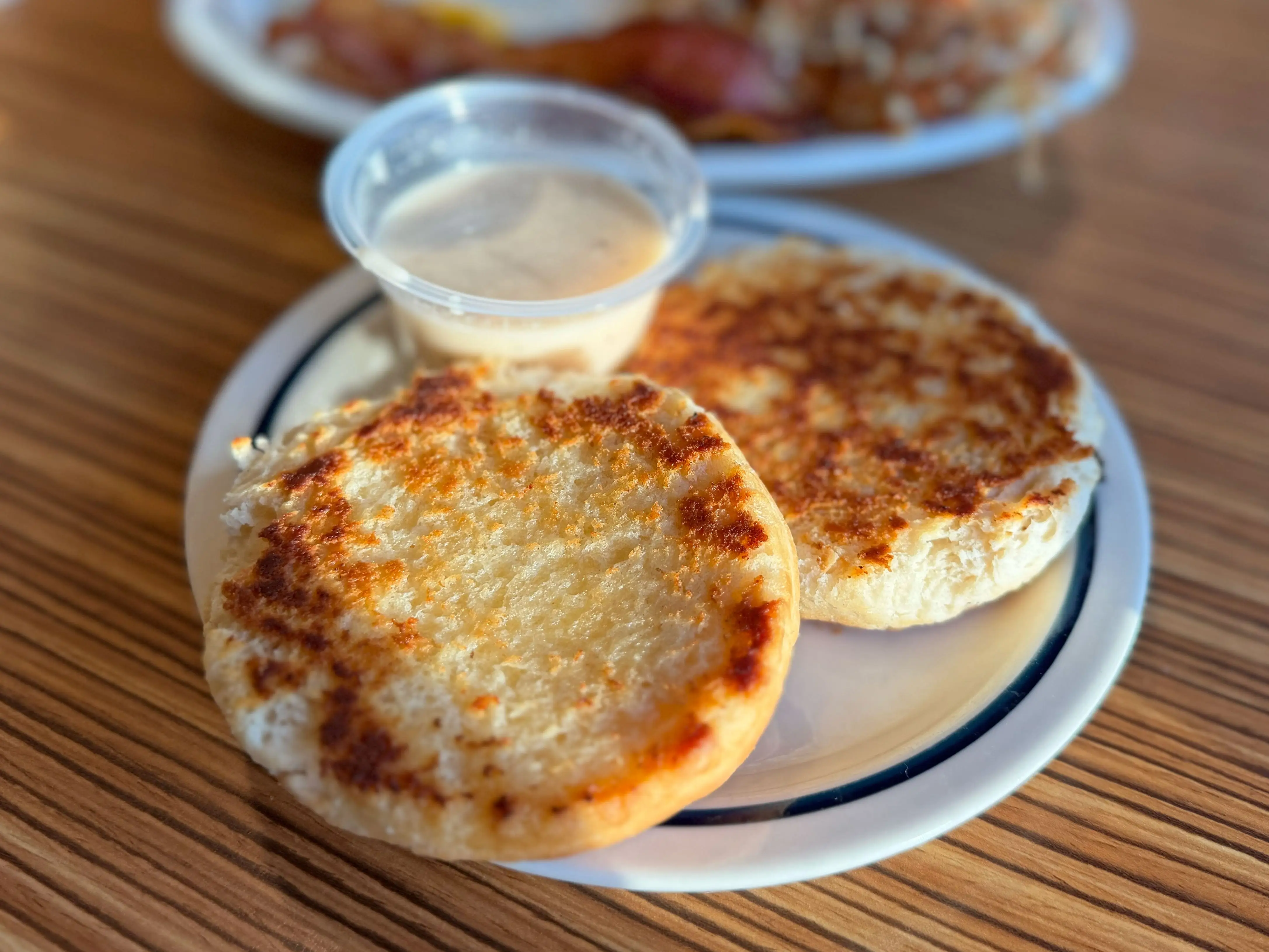 Both sides of a sliced biscuit on a plate with a side of white gravy.