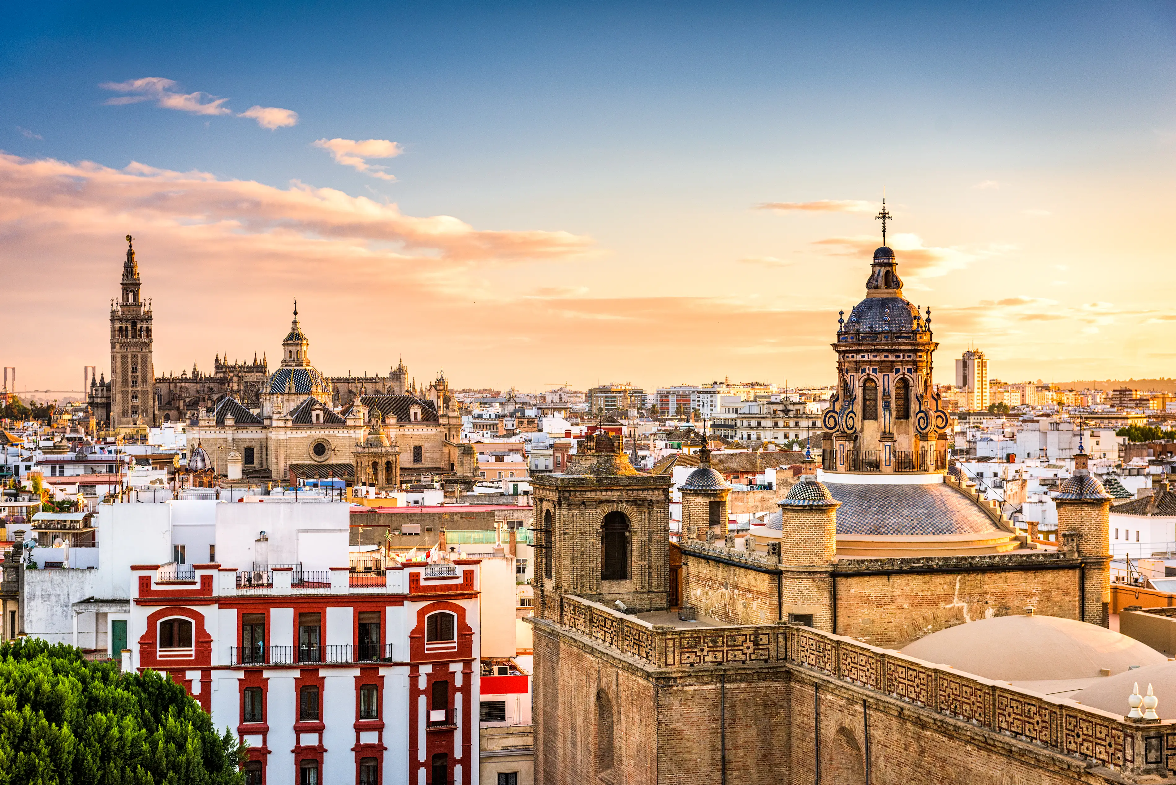 Seville skyline at sunset with the Giralda tower, Seville Cathedral, rooftops, and historic church domes.