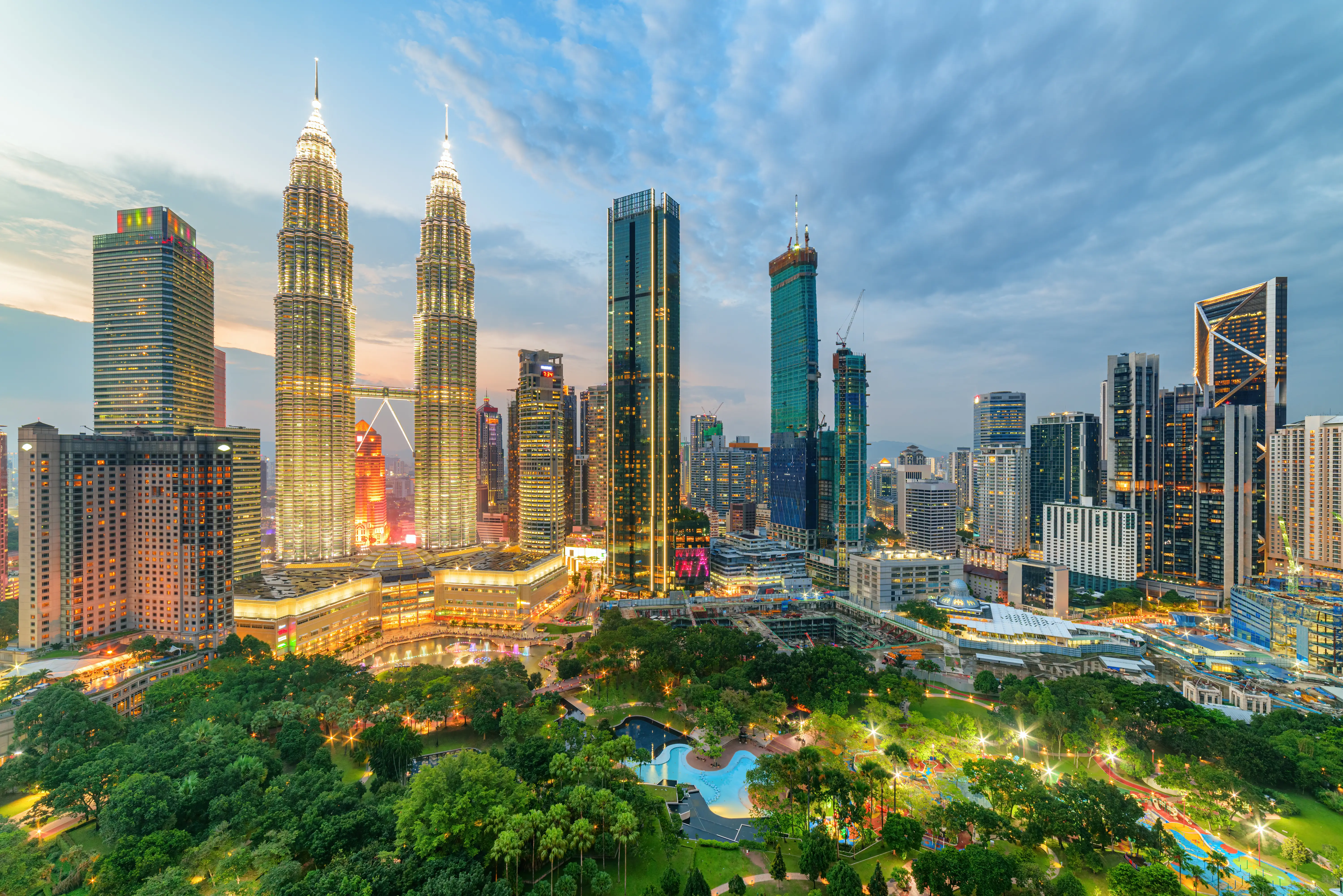 Kuala Lumpur skyline at dusk with Petronas Twin Towers rising above skyscrapers and KLCC Park.