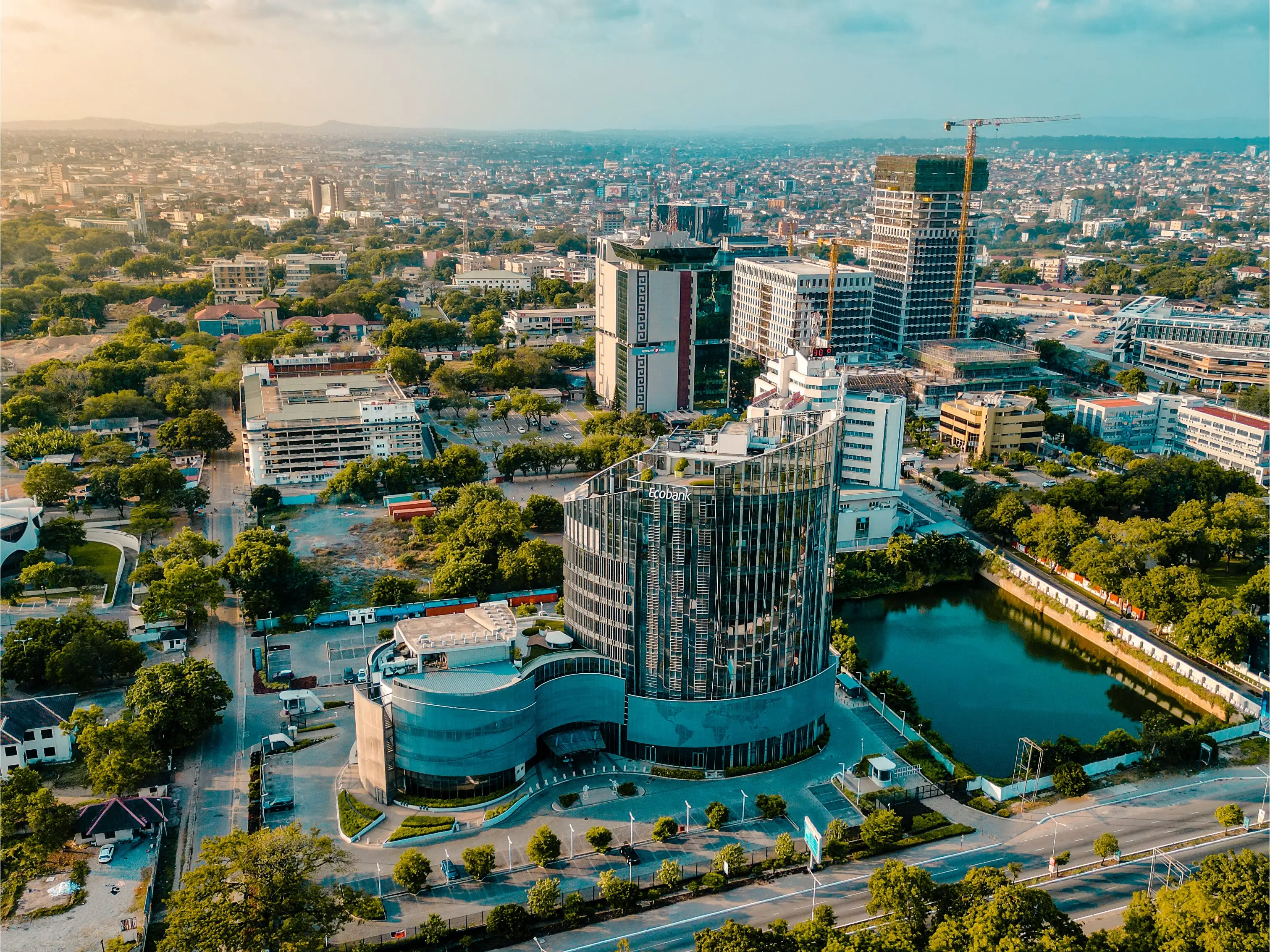 Aerial view of a modern city district with high-rise buildings, tree-lined roads, and a small urban lake.