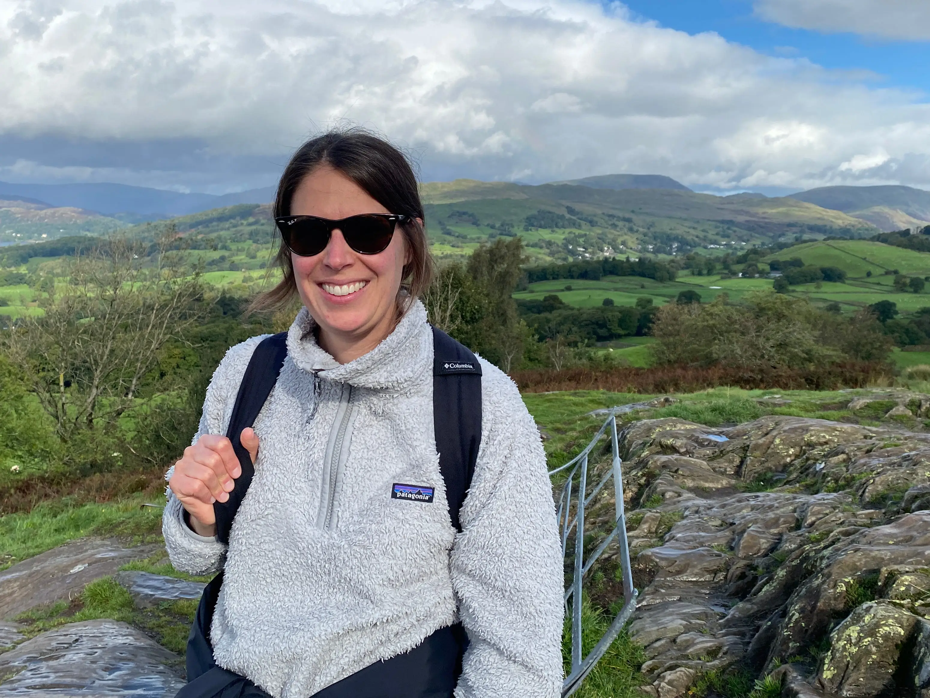Woman with backpack smiling, views of treetops and sky behind her