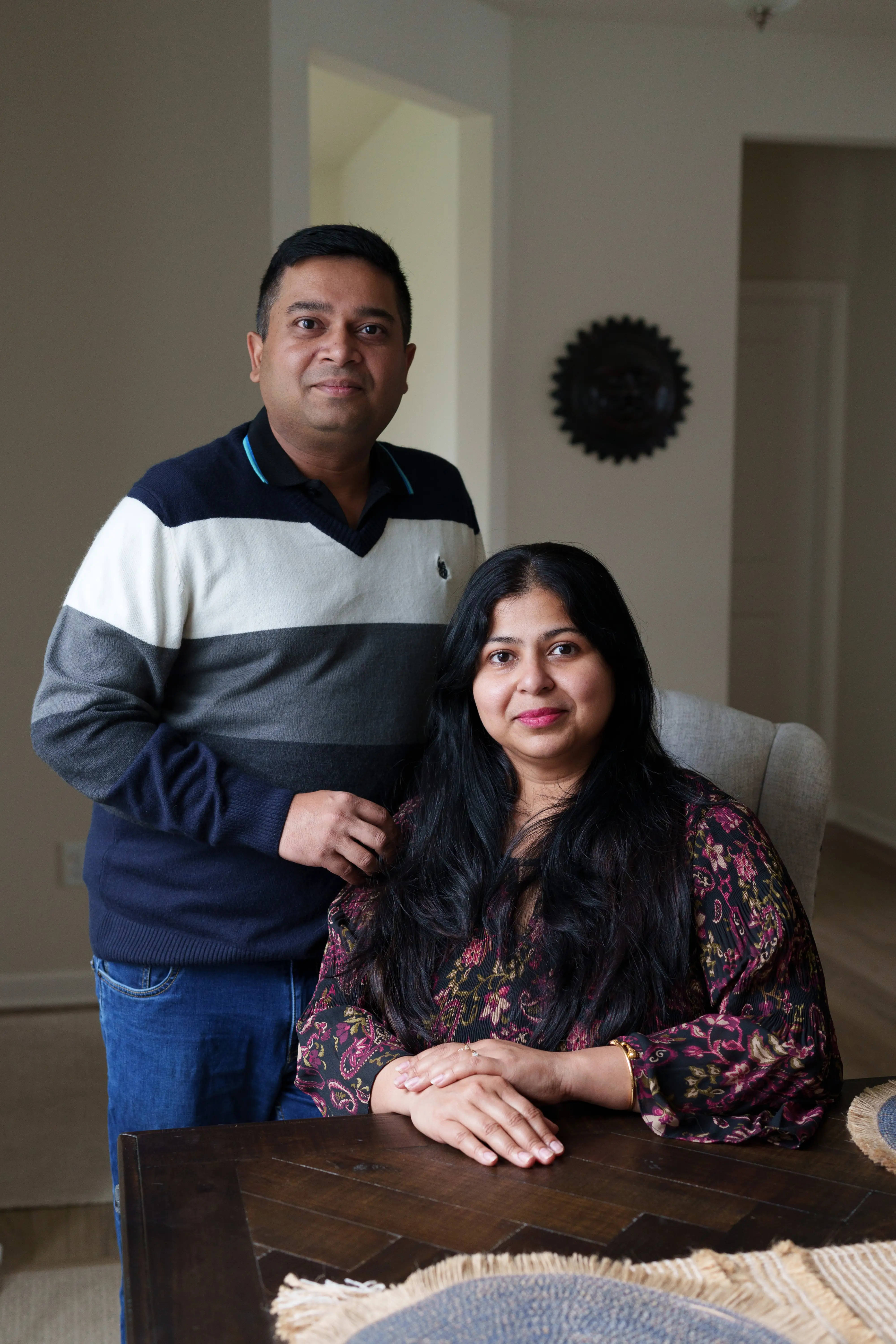 Two people pose together at a dining table in a softly lit home interior.