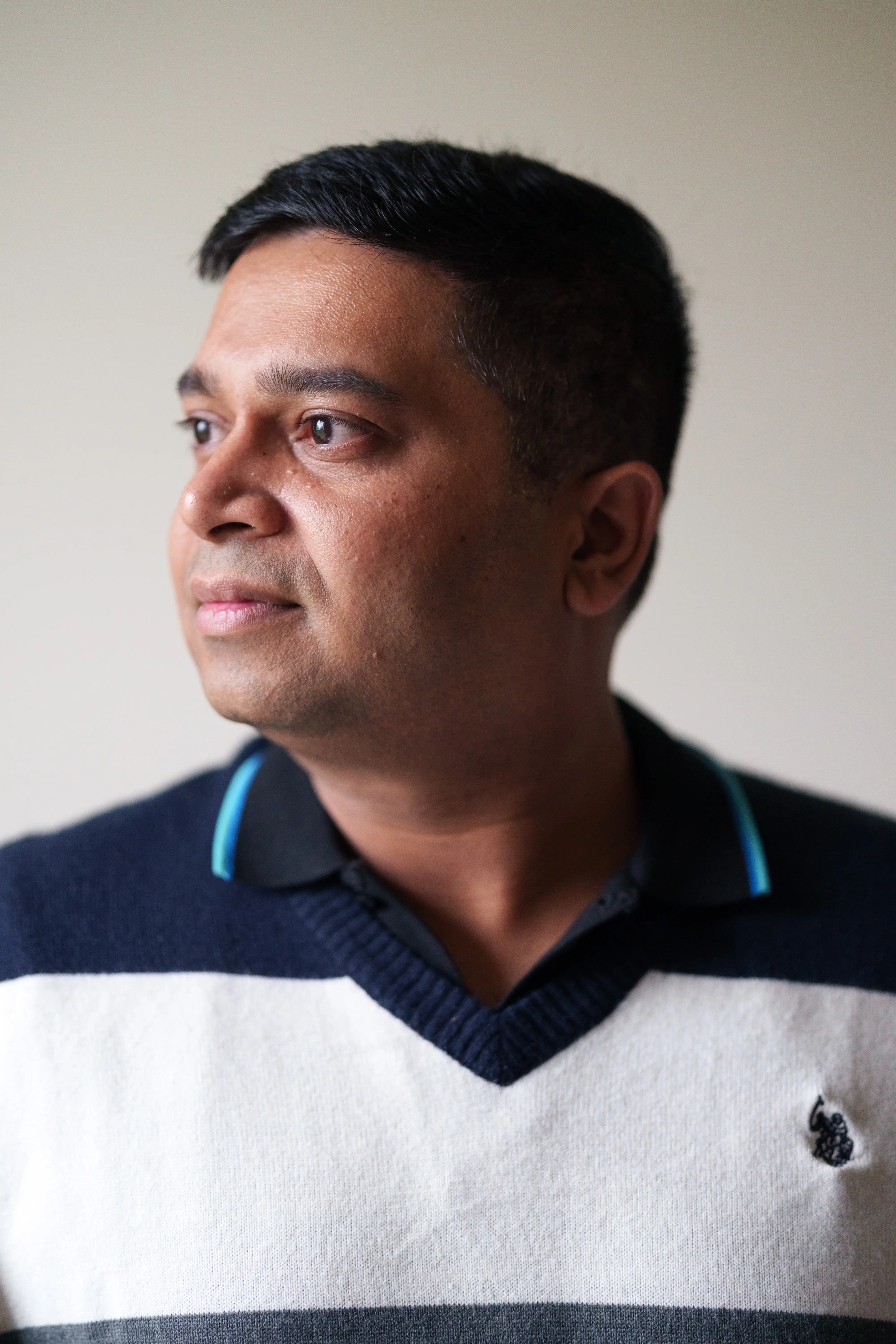 Person in a striped sweater looks to the side against a plain indoor background.