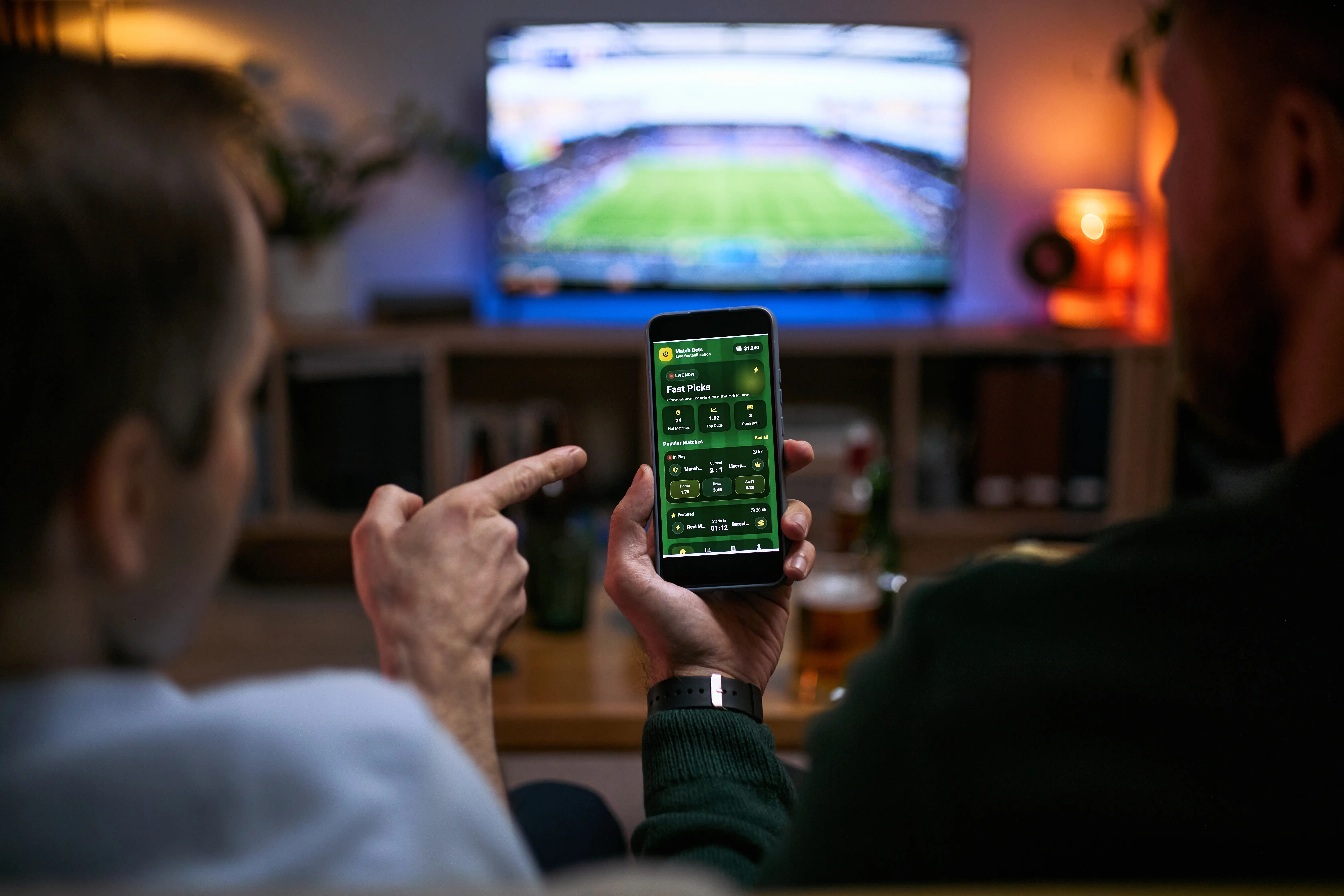 Two people watch a televised soccer match while viewing a bet365 sports betting app on a smartphone.