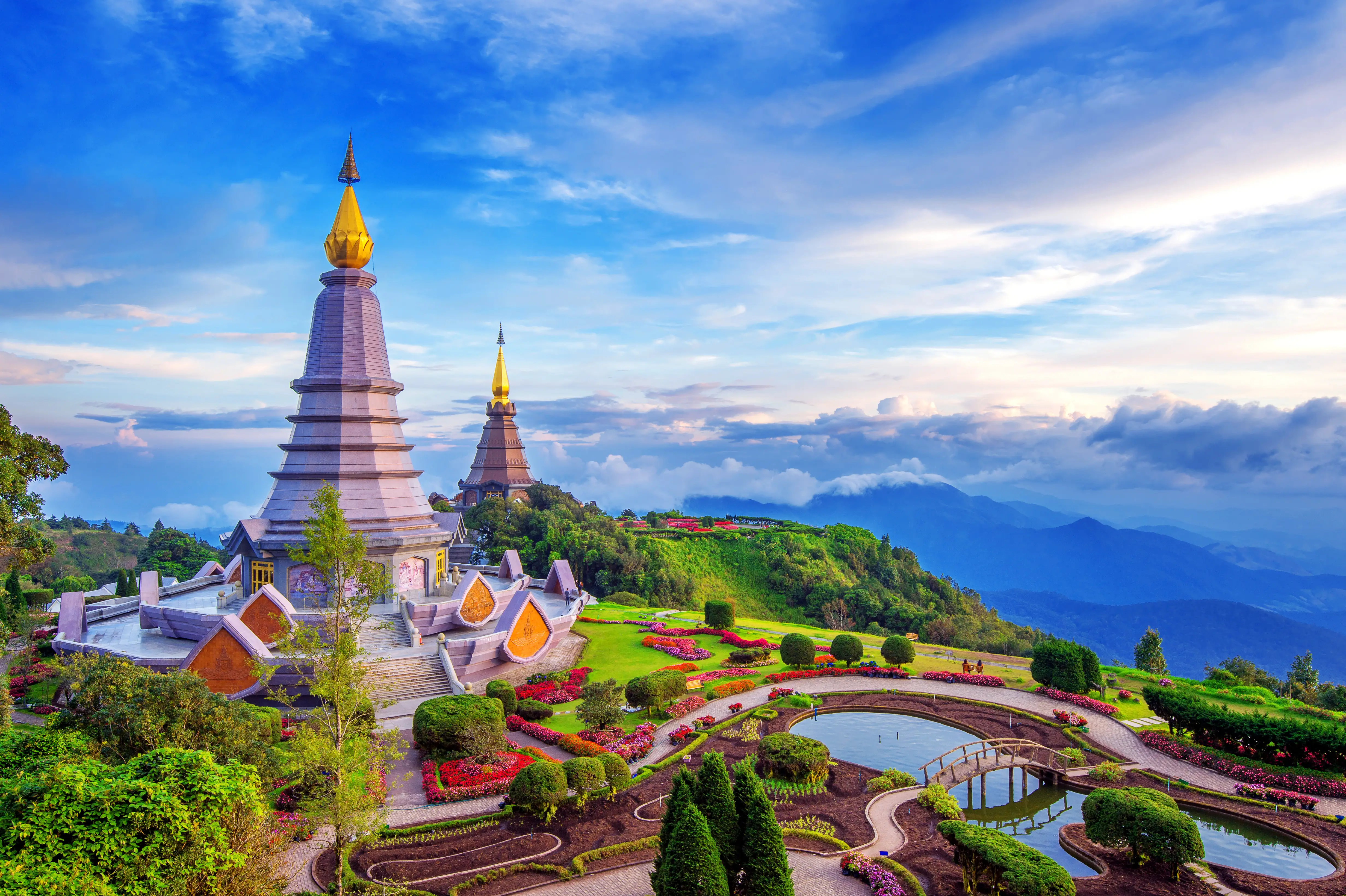 Twin pagodas rise above landscaped gardens on a mountain ridge under a colorful evening sky.