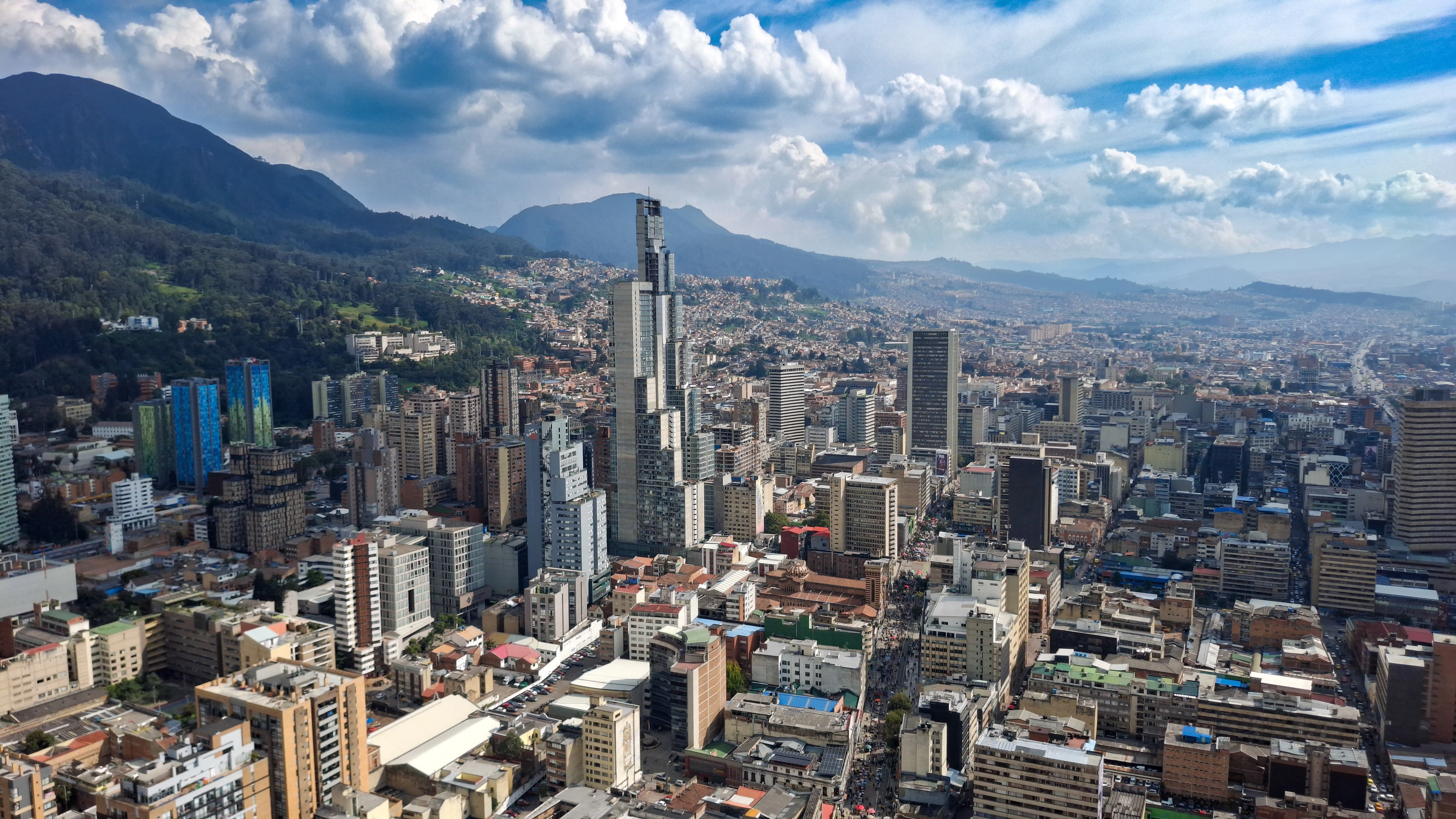 Panoramic aerial view of Bogotá, Colombia, surrounded by a dense city skyline, with the Andes mountains in the background.