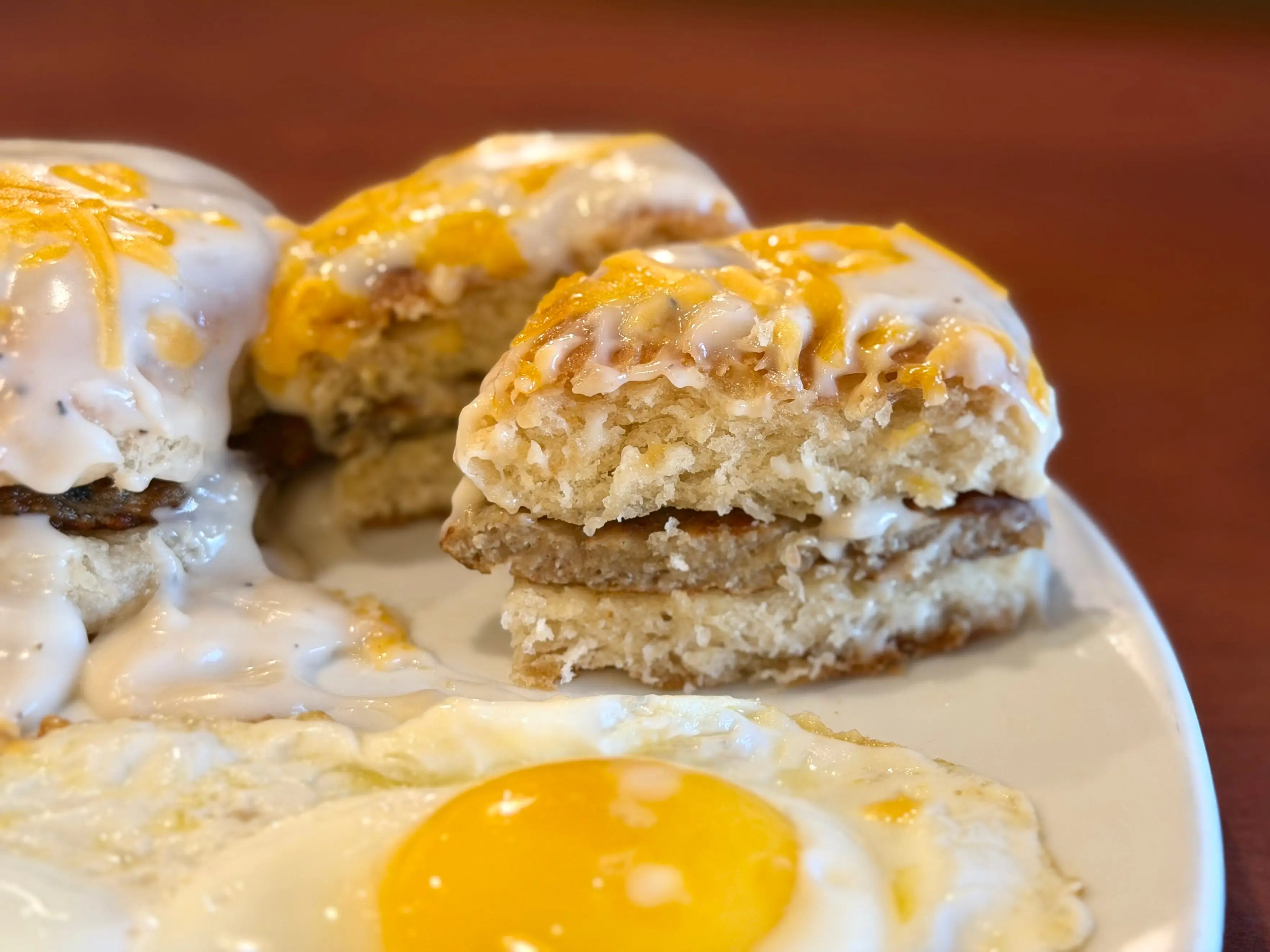 Two halves of a biscuit, each with a sausage patty, white gravy, and shreds of American cheese.