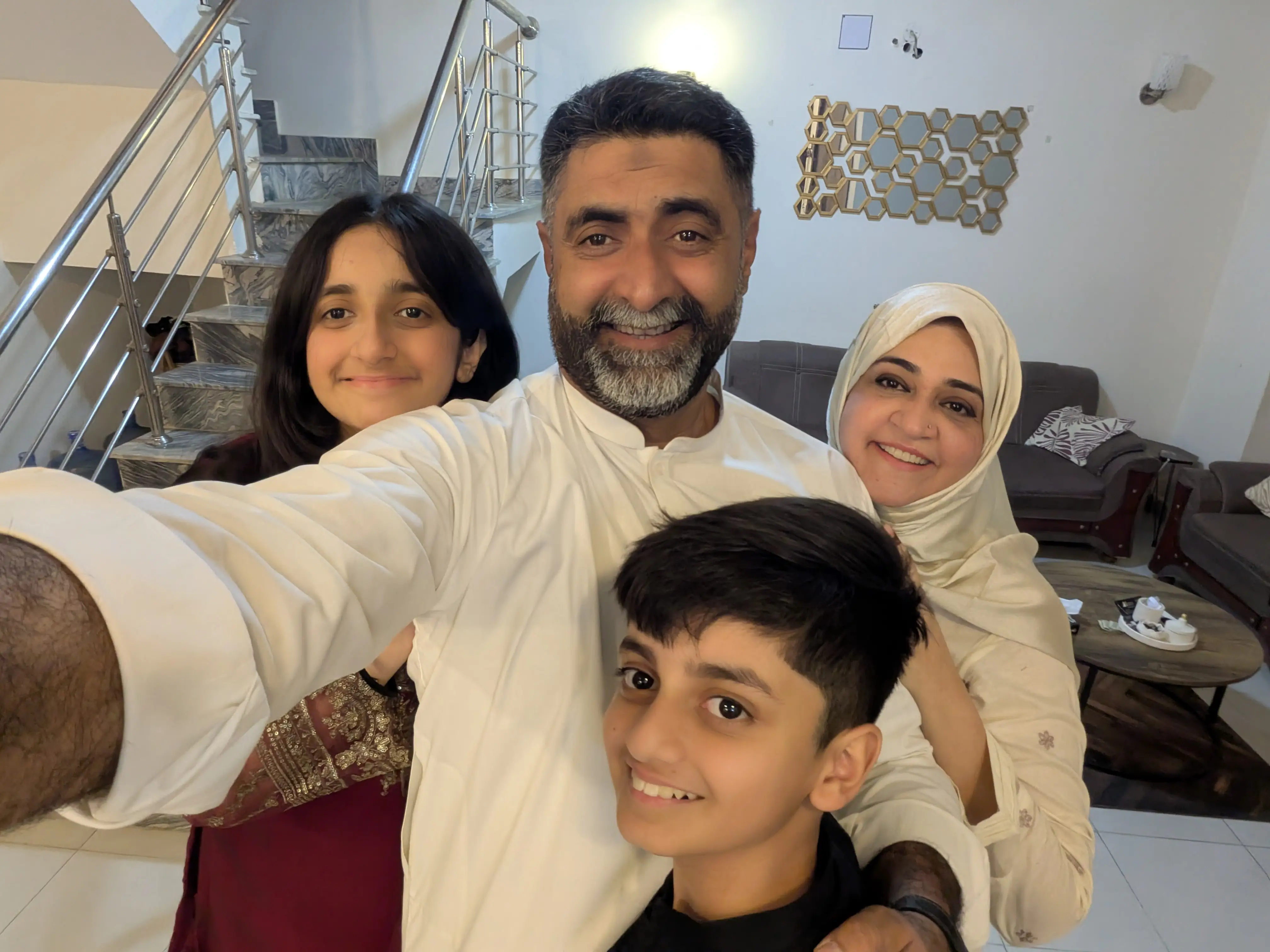 Four smiling people pose for a close selfie in a living room beside a staircase.