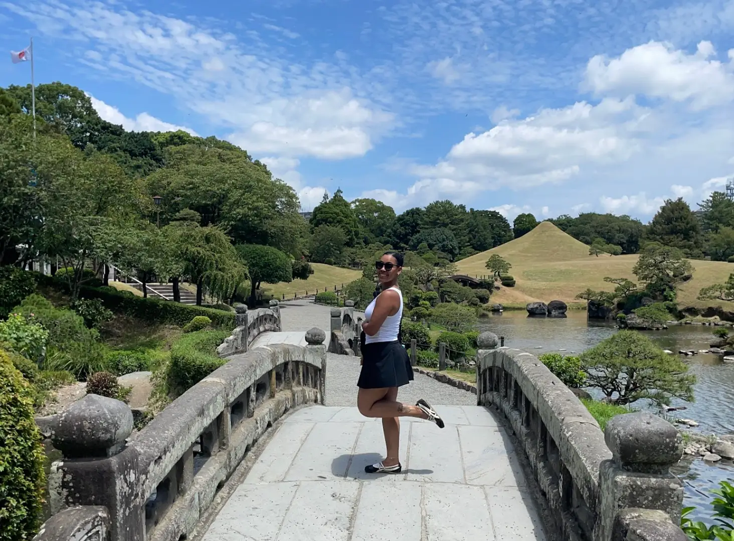 The writer stands on a bridge in Japan, with a flag visible in the background and water and greenery nearby.