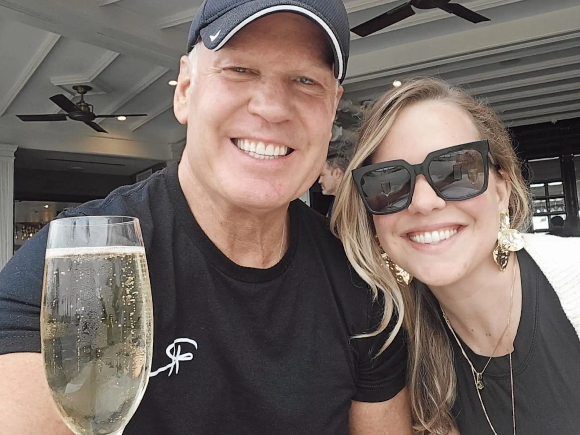 A man smiles with his daughter at a restaurant table beside a flute of sparkling wine.
