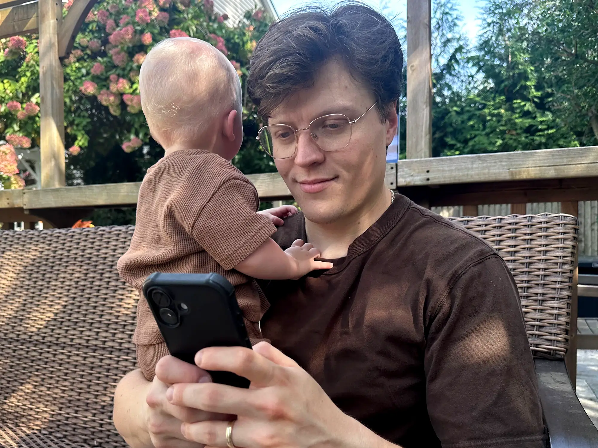 Alex Nicoll looking at his phone and holding his son.