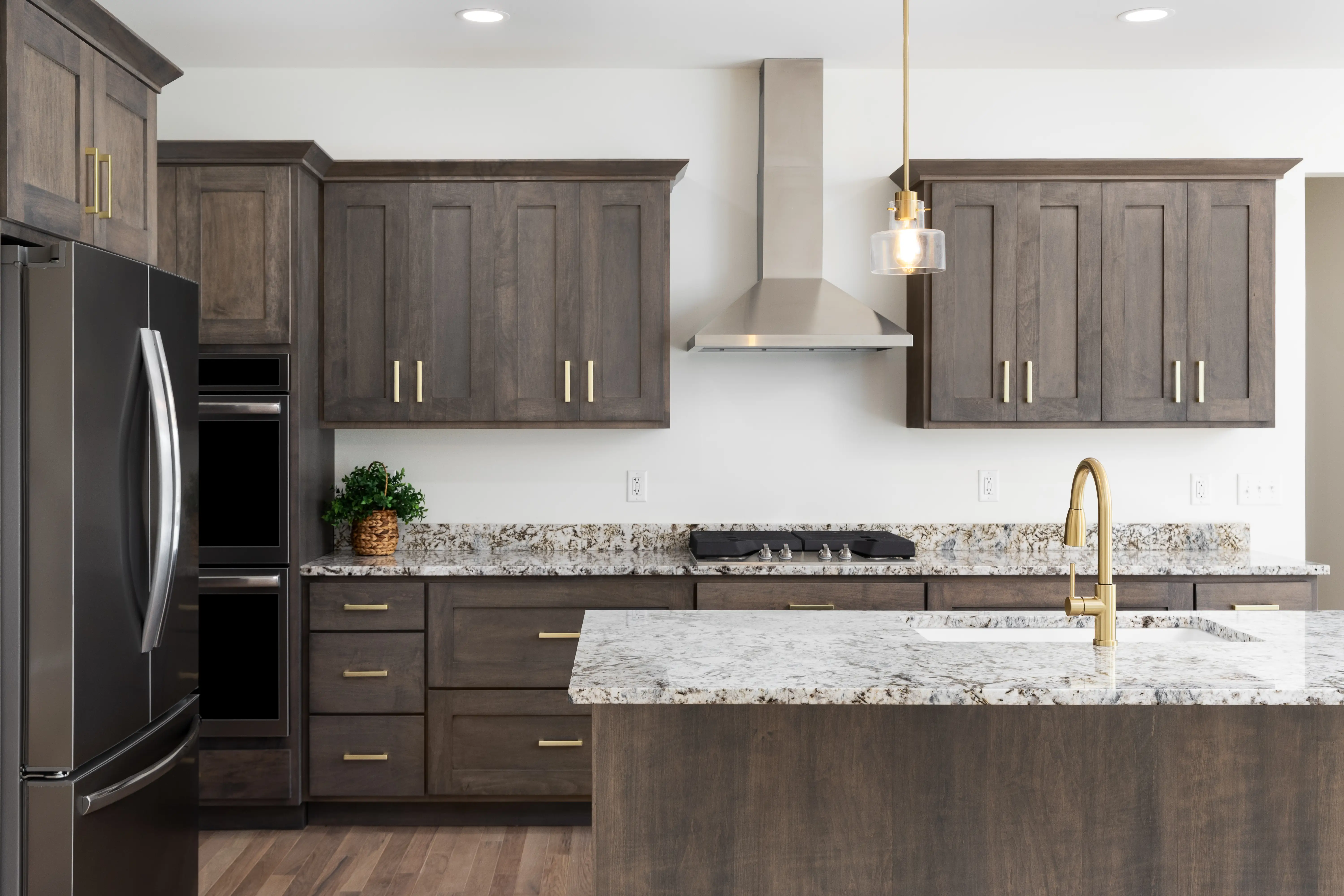 A kitchen with a gold faucet on a granite countertop,dark wood cabinets, stainless steel appliances, and gold pendant lights hanging above the island.