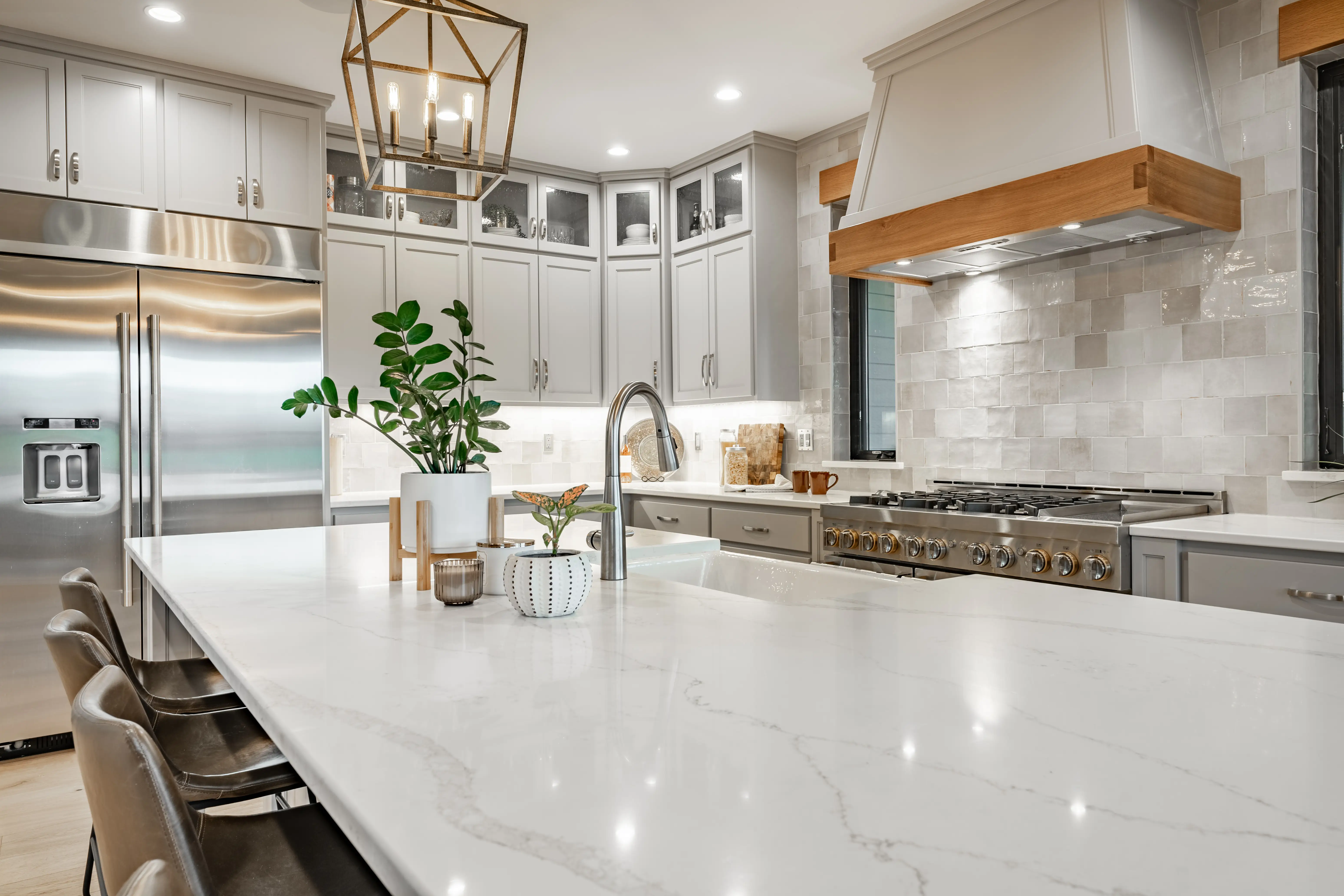 Large kithchen with white countertops, grey cabinets,  large range hood above stove