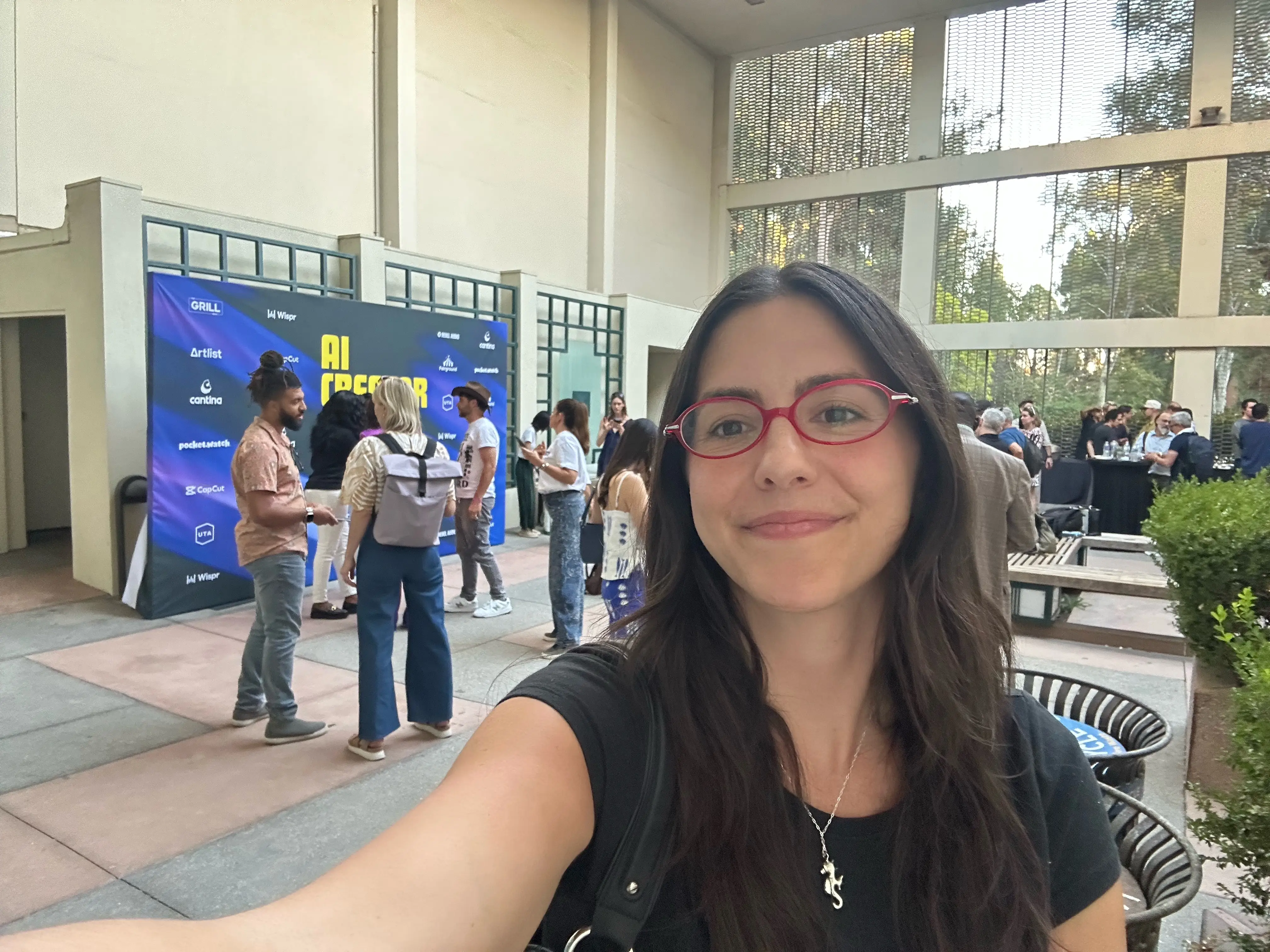 Author taking a selfie at an indoor event entrance with an AI CREATOR sponsor backdrop behind them.