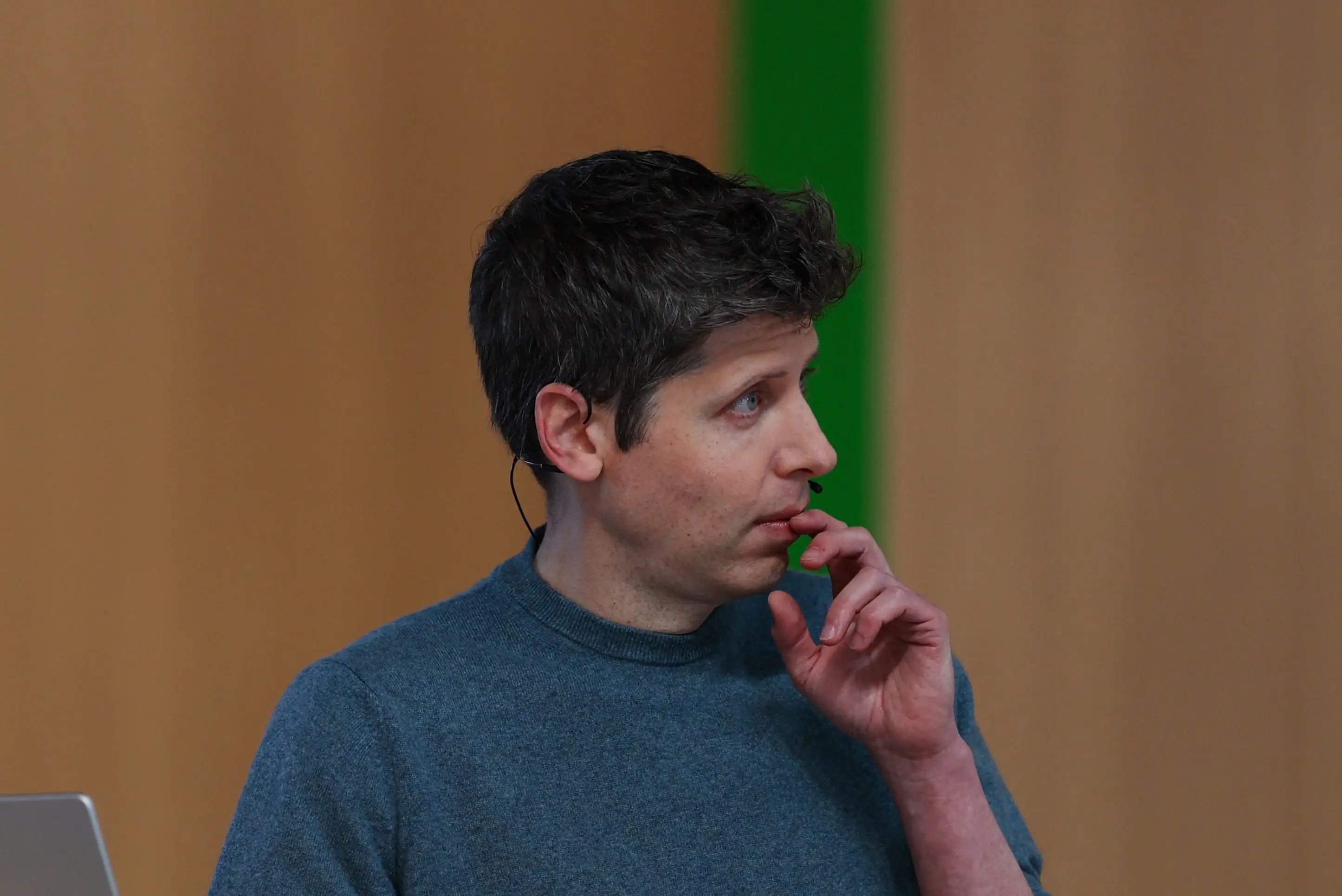 Sam Altman stands at a wooden lectern with an Apple laptop and smartphone.
