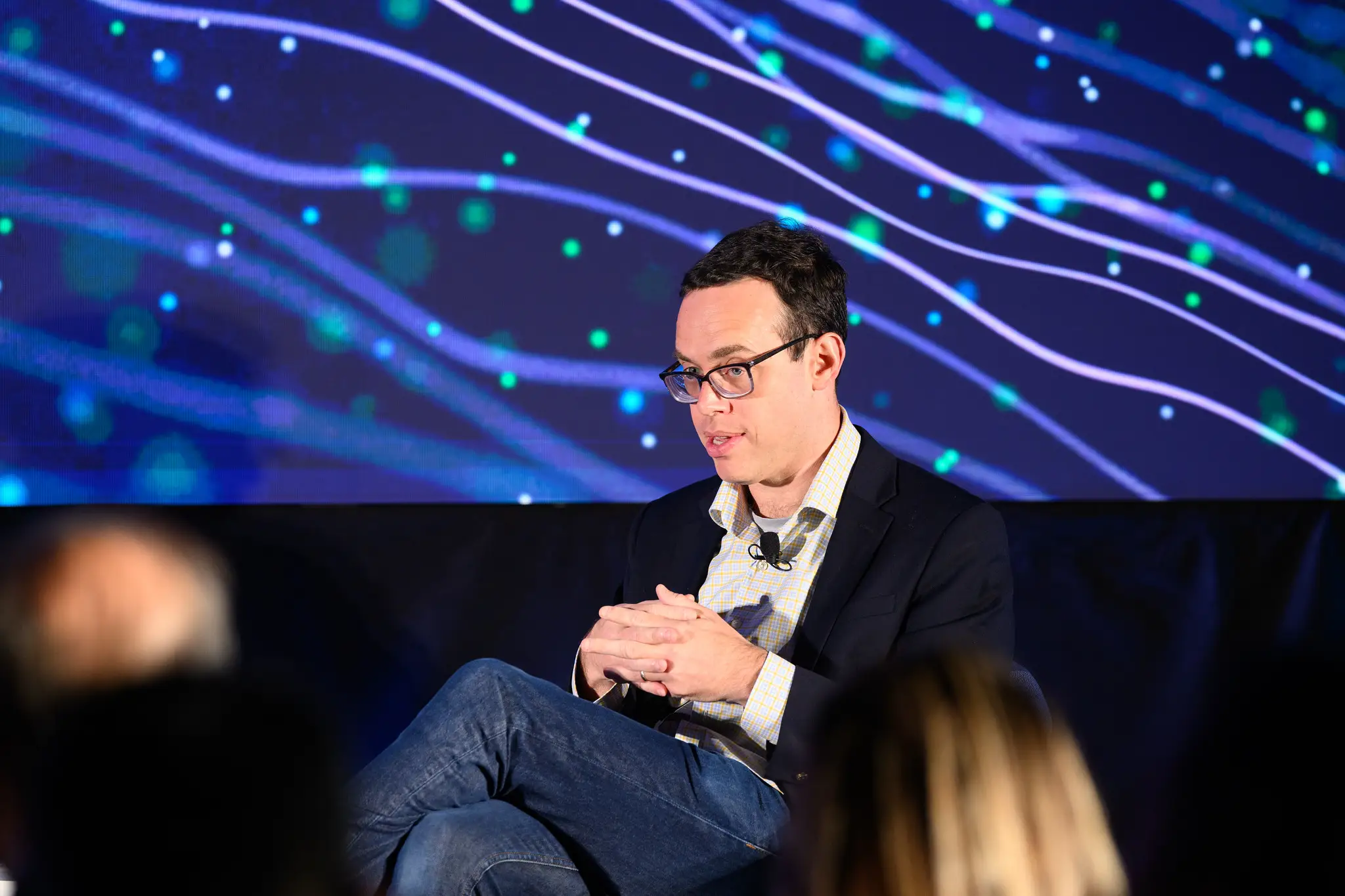David Robinson sits onstage before an abstract blue and green digital backdrop during a conference session.