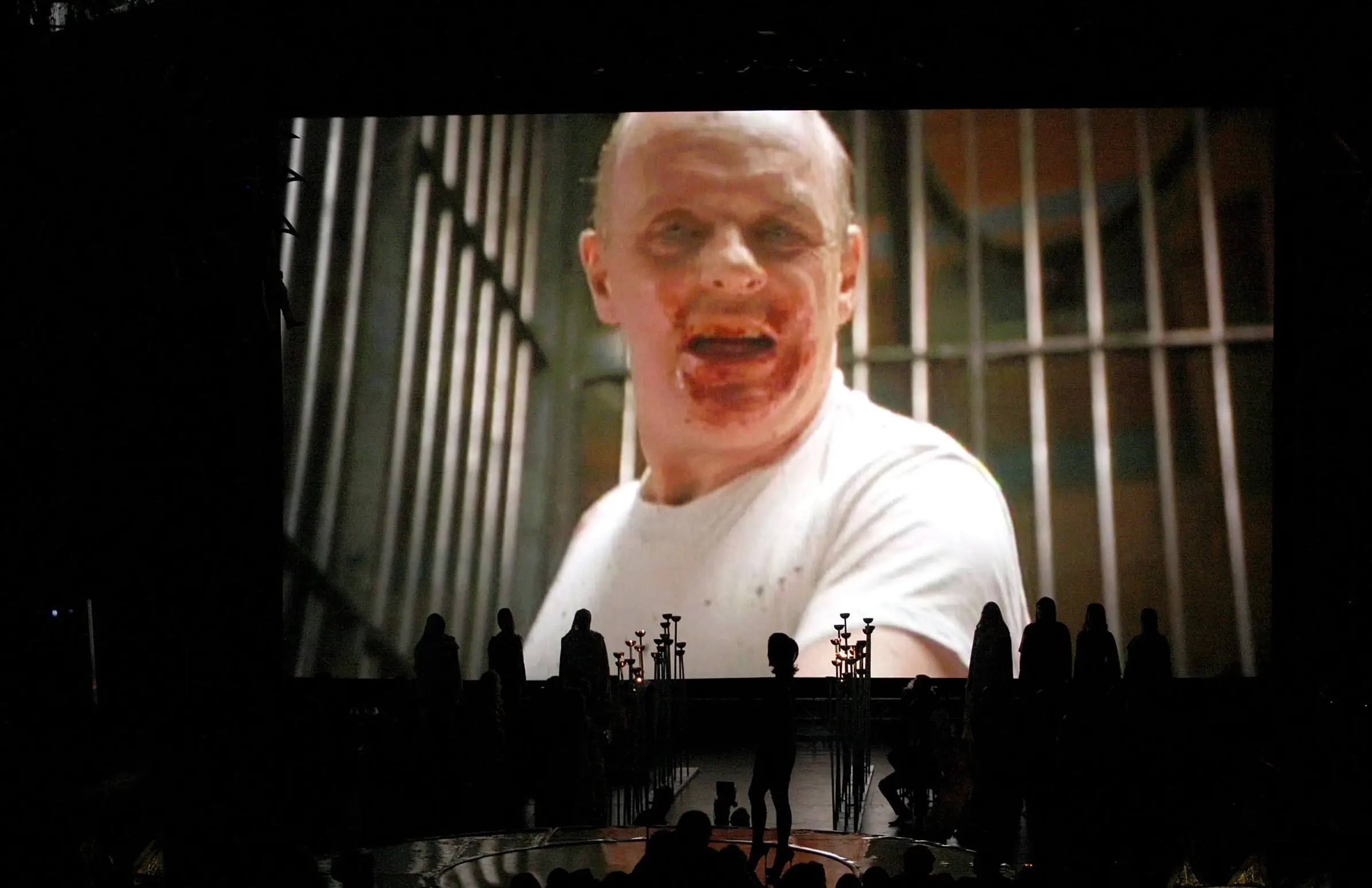 Anthony Hopkins in a film scene with bars behind him and blood on his face.