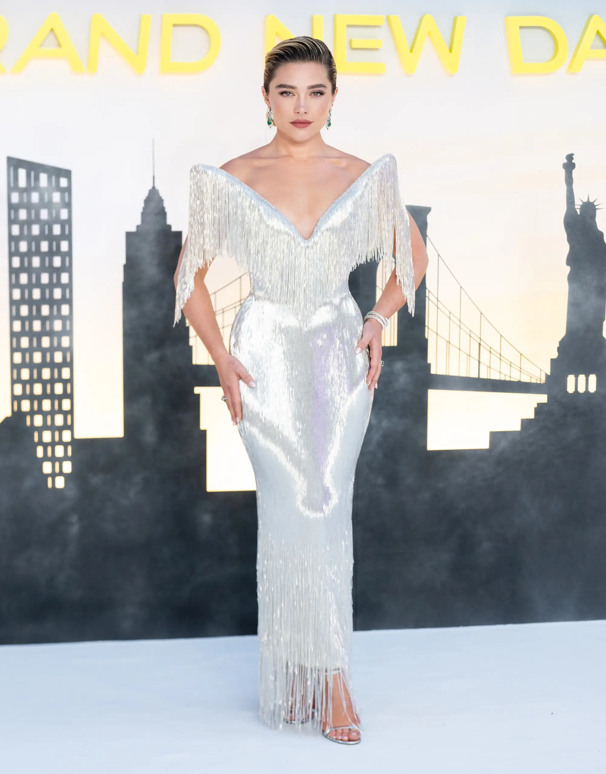 Florence Pugh poses in a silver fringed gown before a New York skyline backdrop.