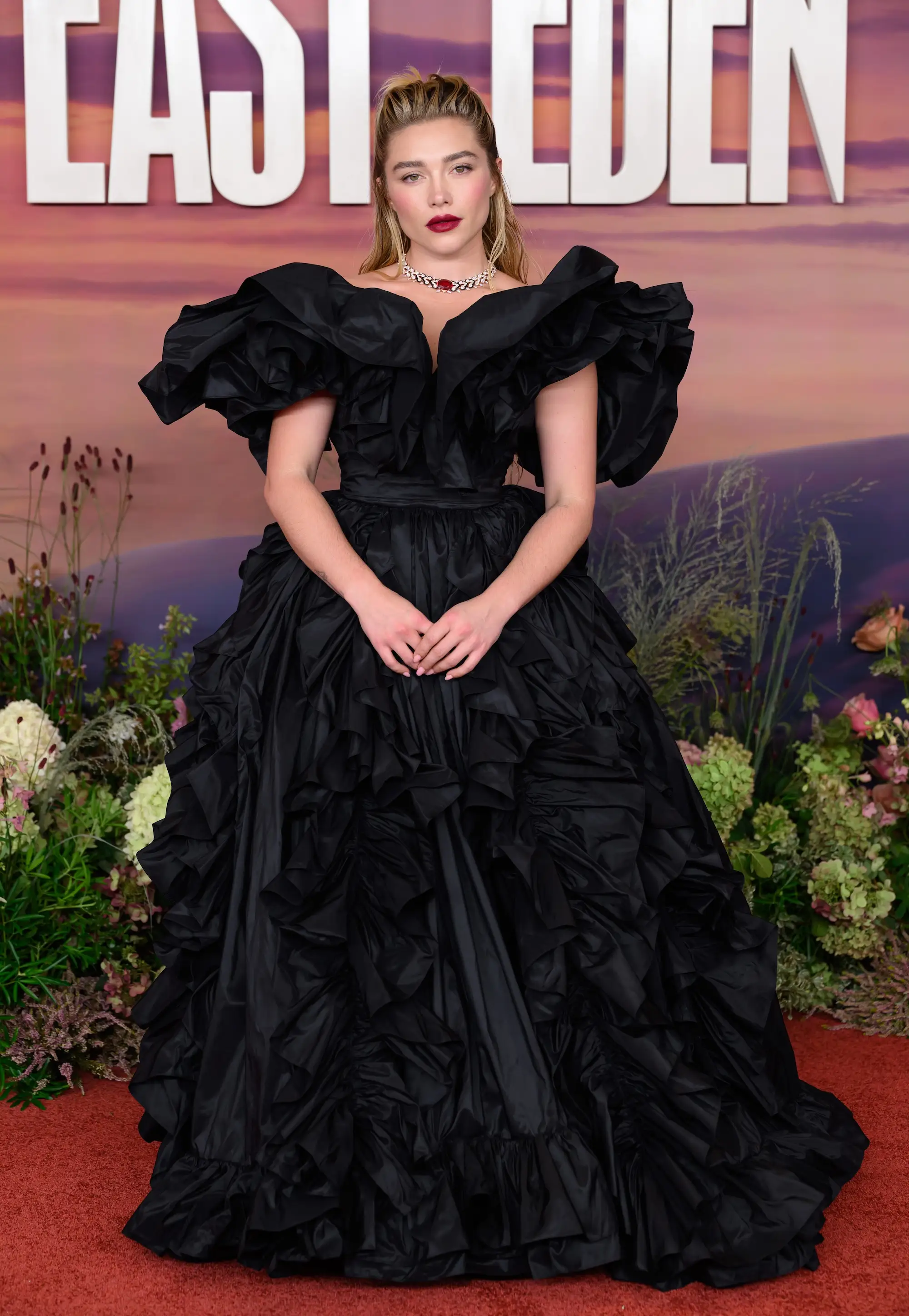 Florence Pugh poses on a red carpet in a black ruffled gown before an
