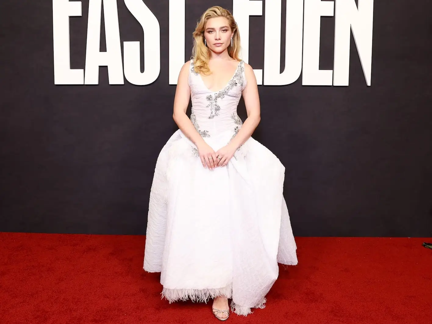 Florence Pugh poses in a white gown on a red carpet before an