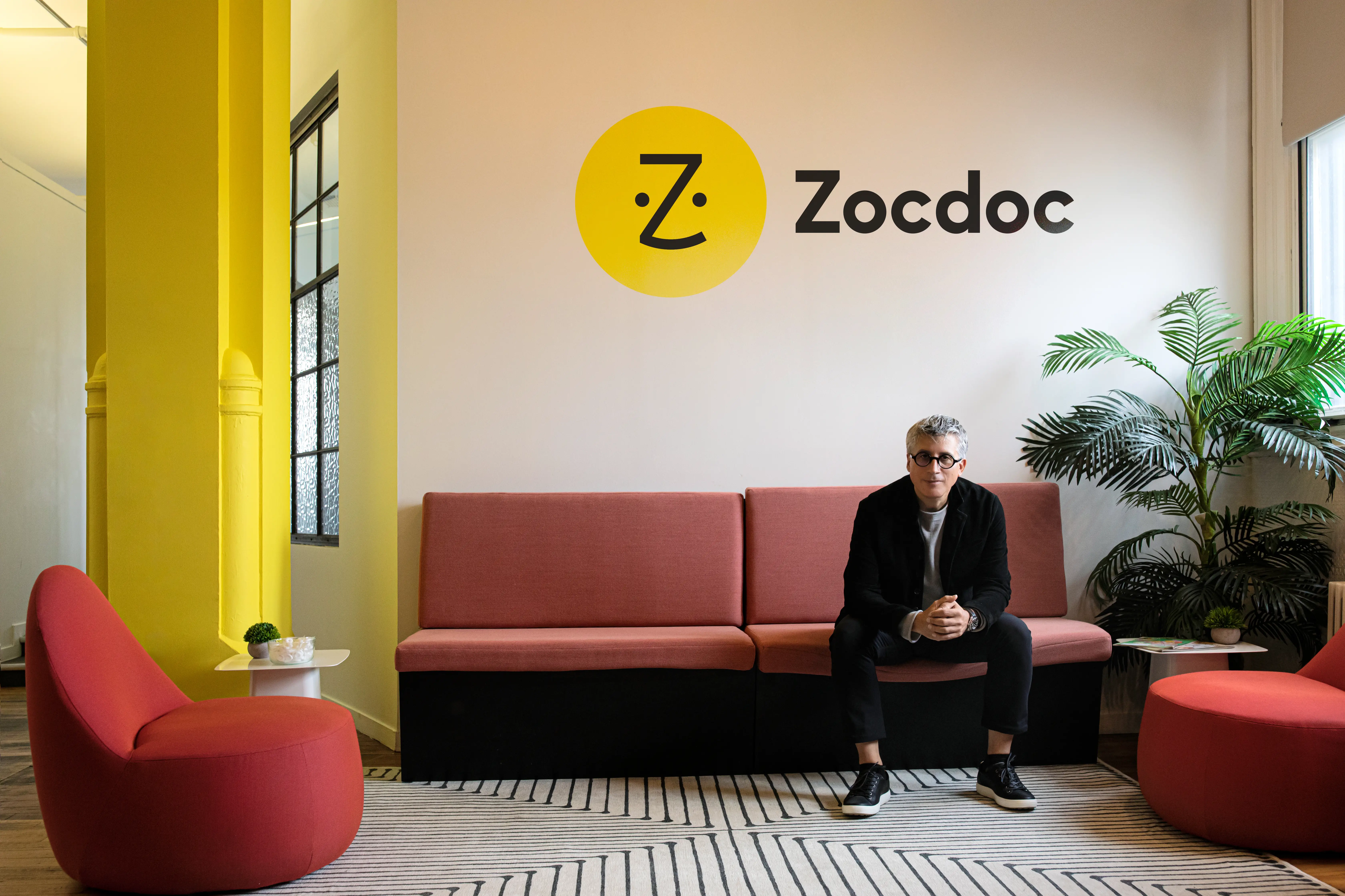 the CEO of Zocdoc poses in front of the logo