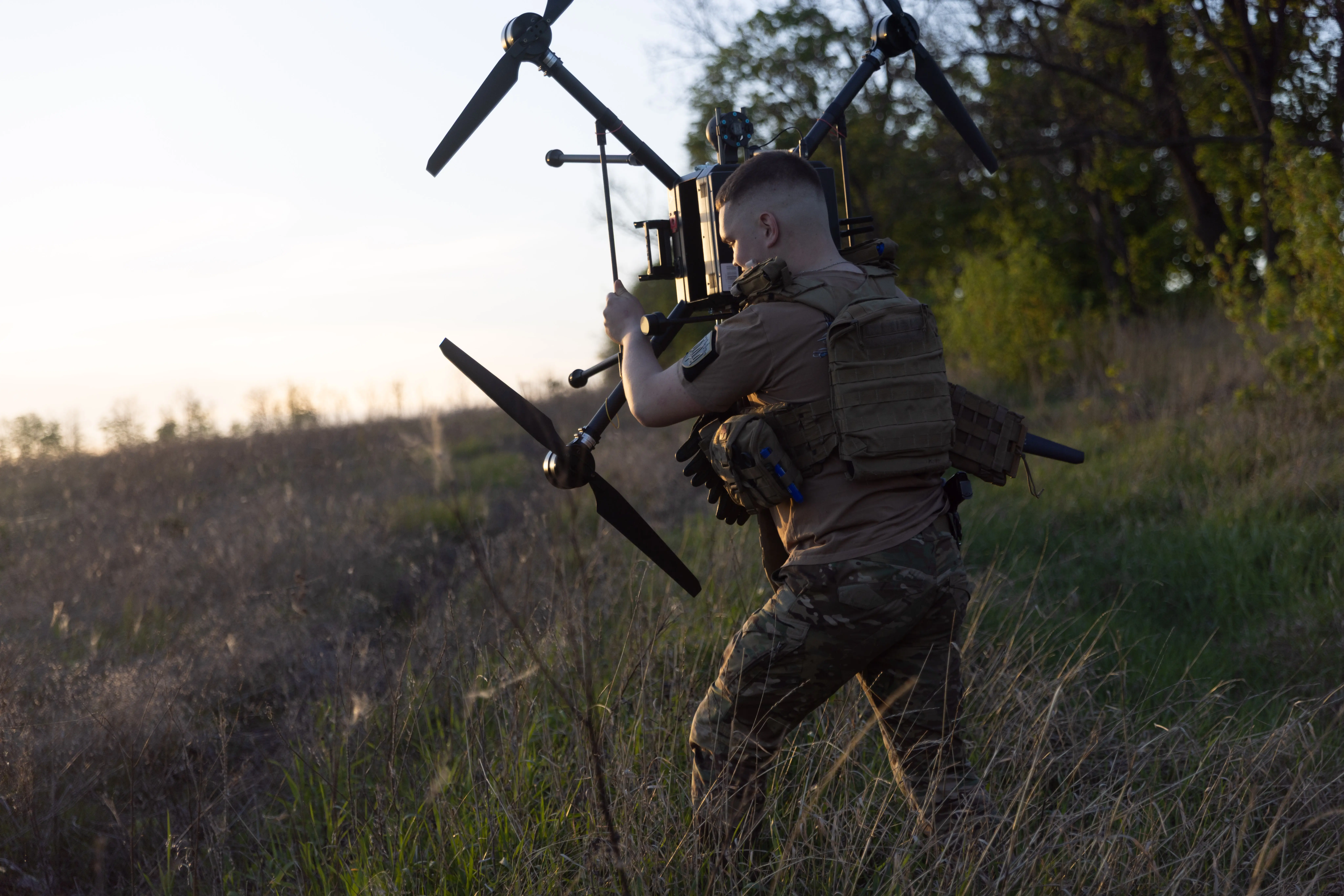A Ukrainian soldier holds a drone in a field.