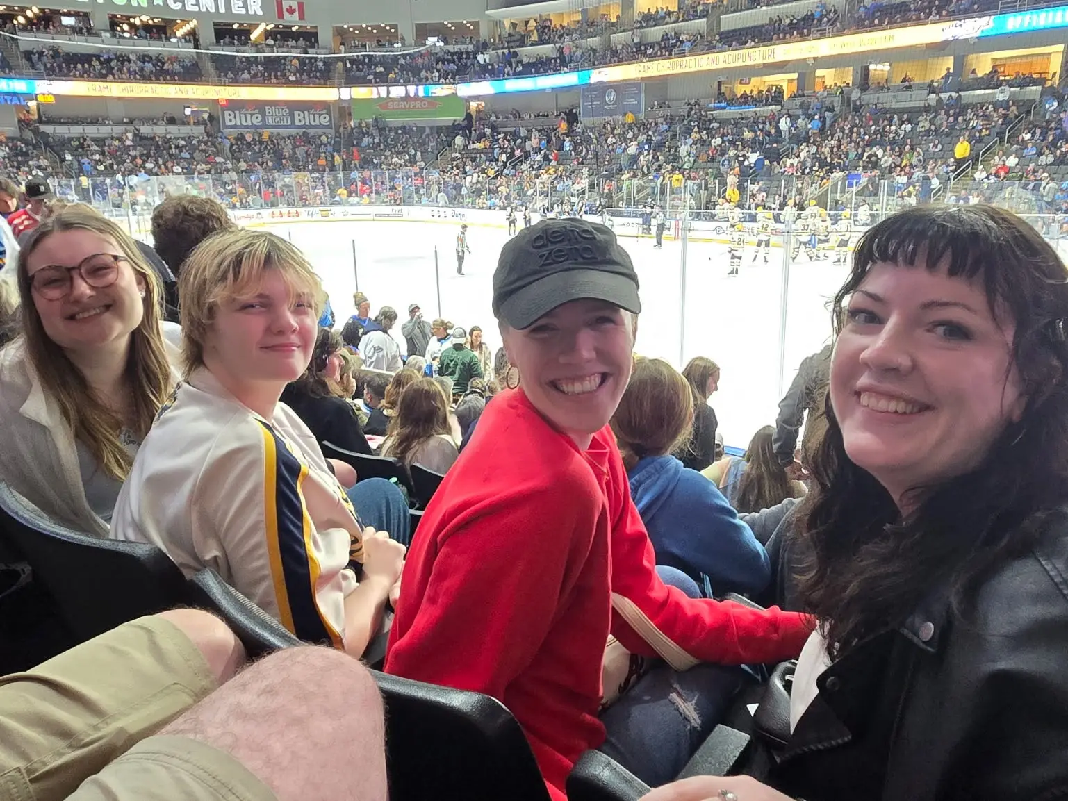 The writer, her girlfriend, and her two other roommates are sitting at a hockey game.