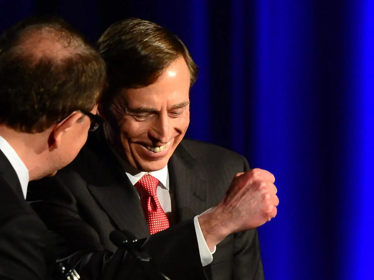 Two suited speakers share a smiling exchange at a lectern bearing the University of Southern California seal.