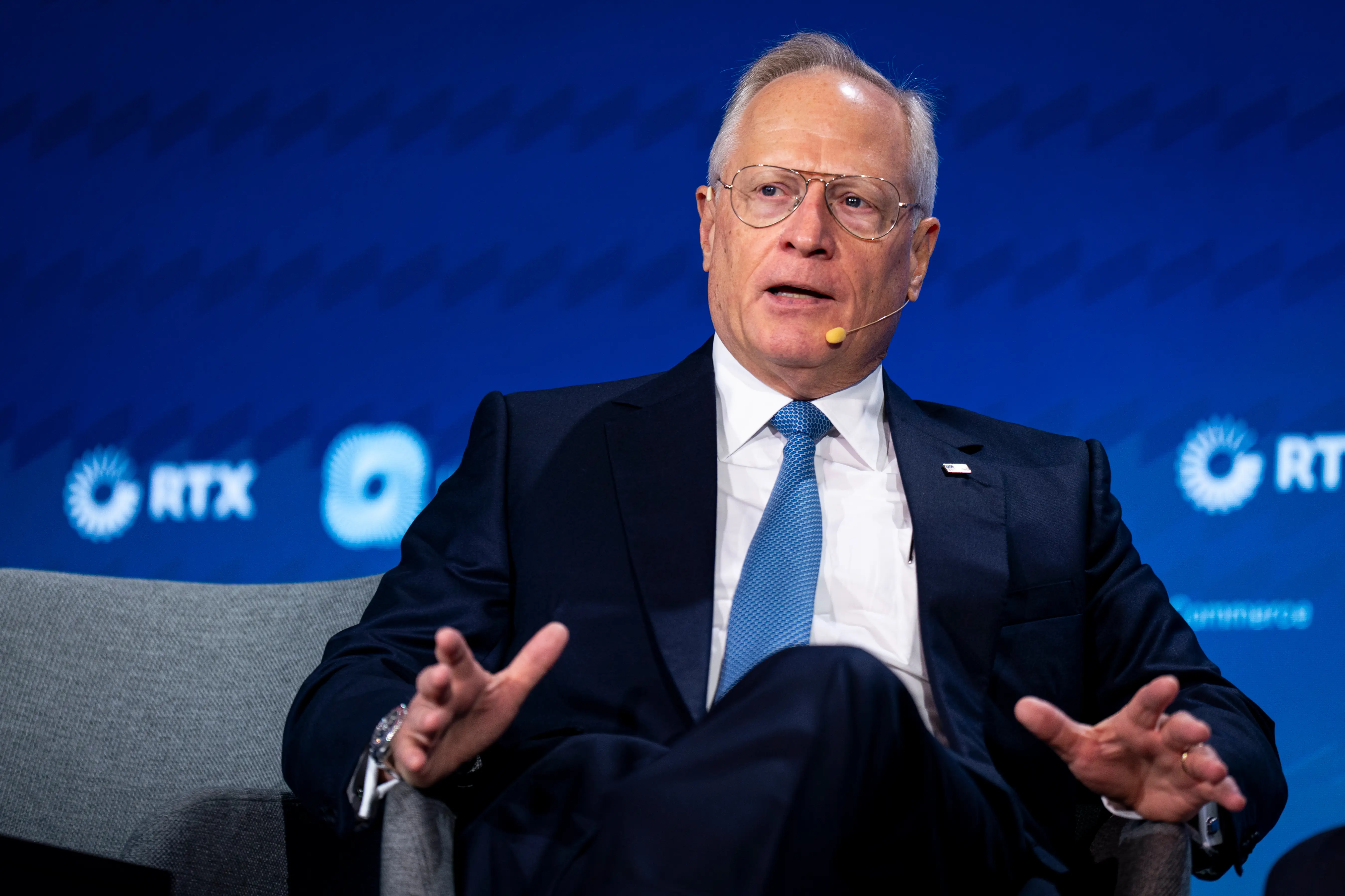 Ross Perot Jr., wearing a headset microphone, sits onstage before a blue RTX backdrop.