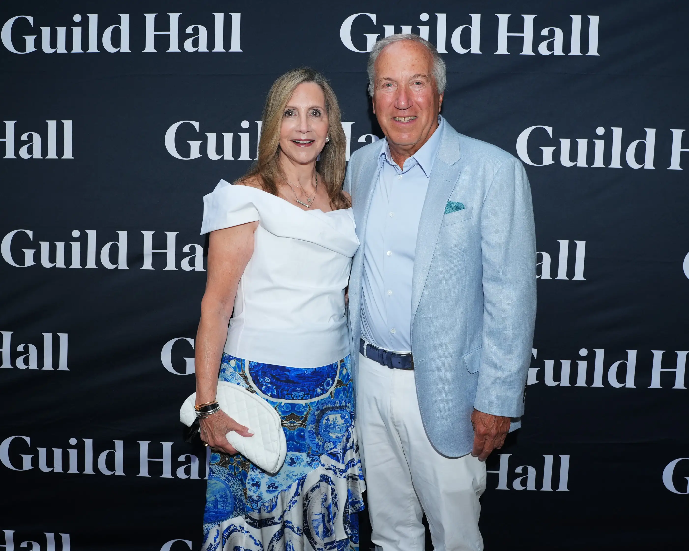 Hilarie and Mitchell Morgan pose together in front of a black Guild Hall step-and-repeat backdrop at an event.
