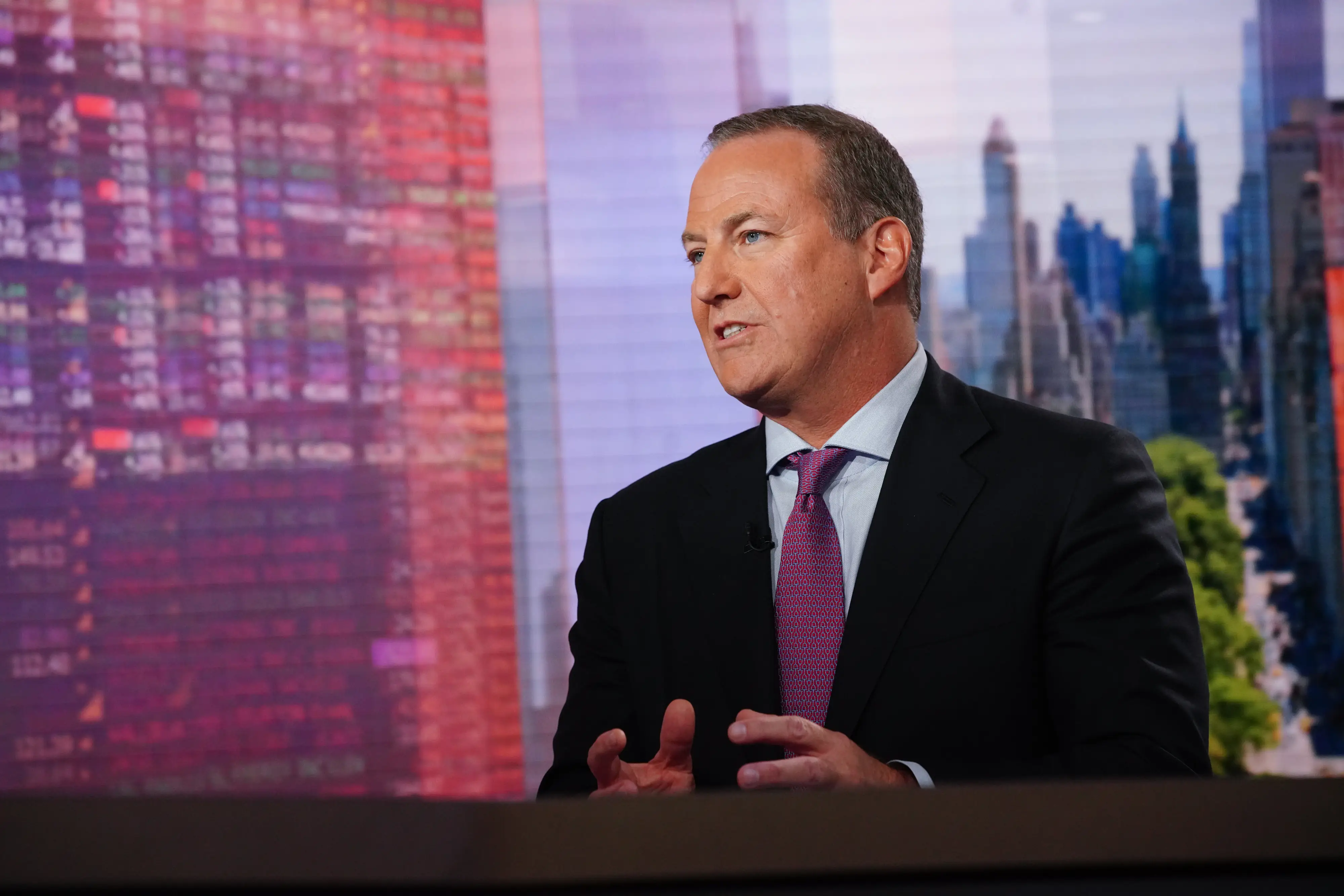 Robert Faith speaks in a studio with a blurred city skyline backdrop.