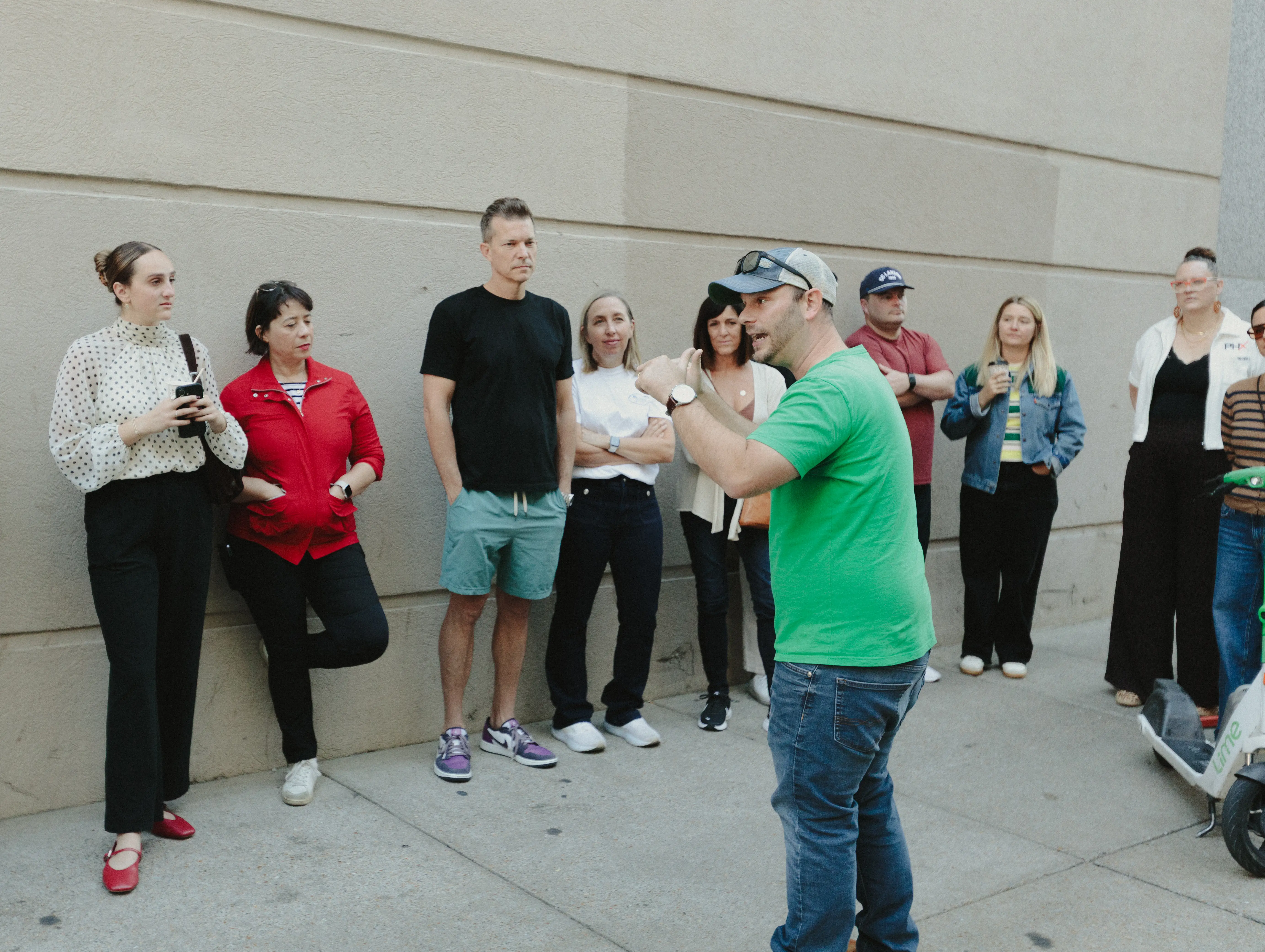 Paul gestures while addressing a small tour group on a city sidewalk.
