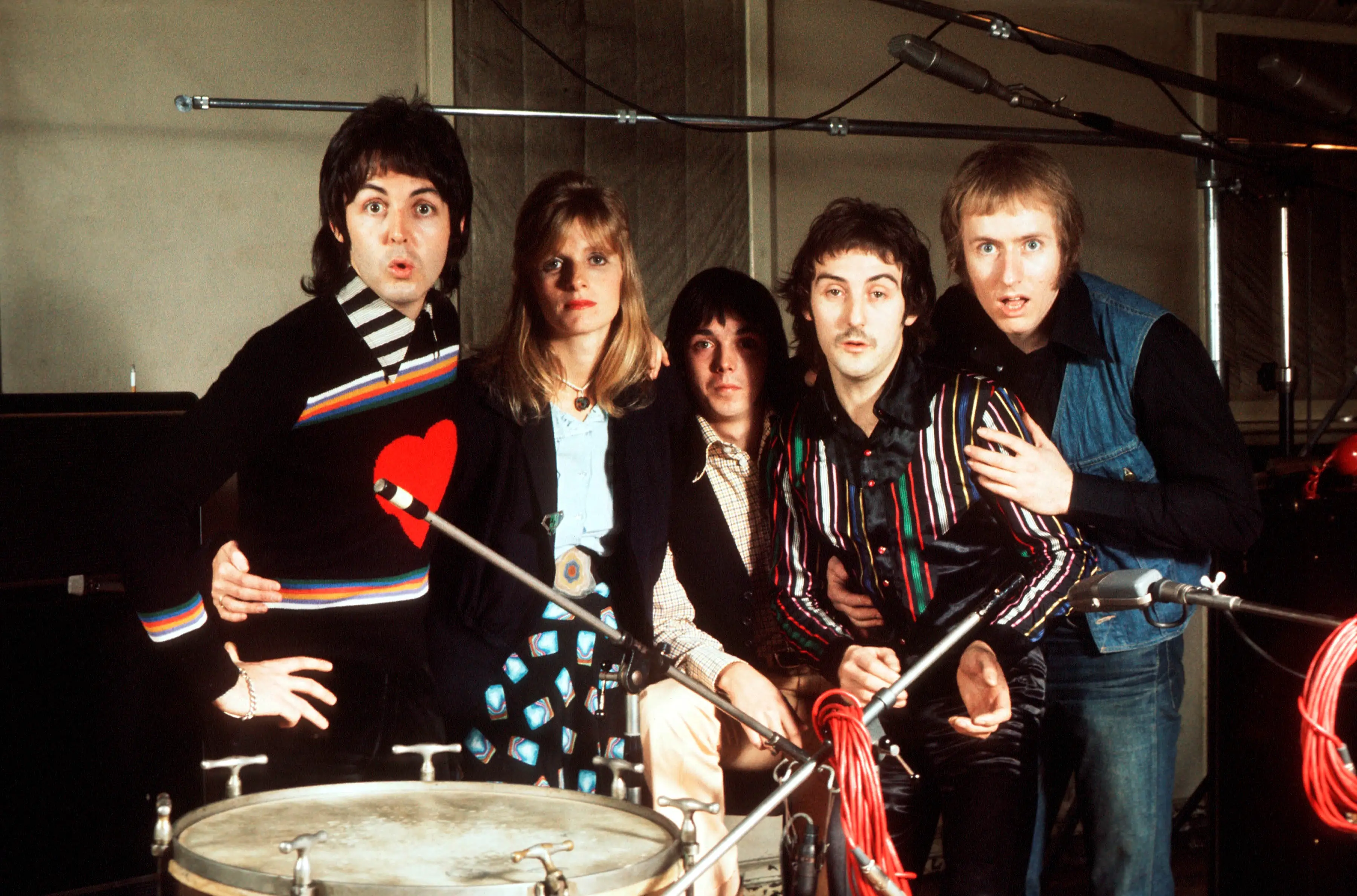 Five band members of Wings pose around a drum kit in a recording studio.