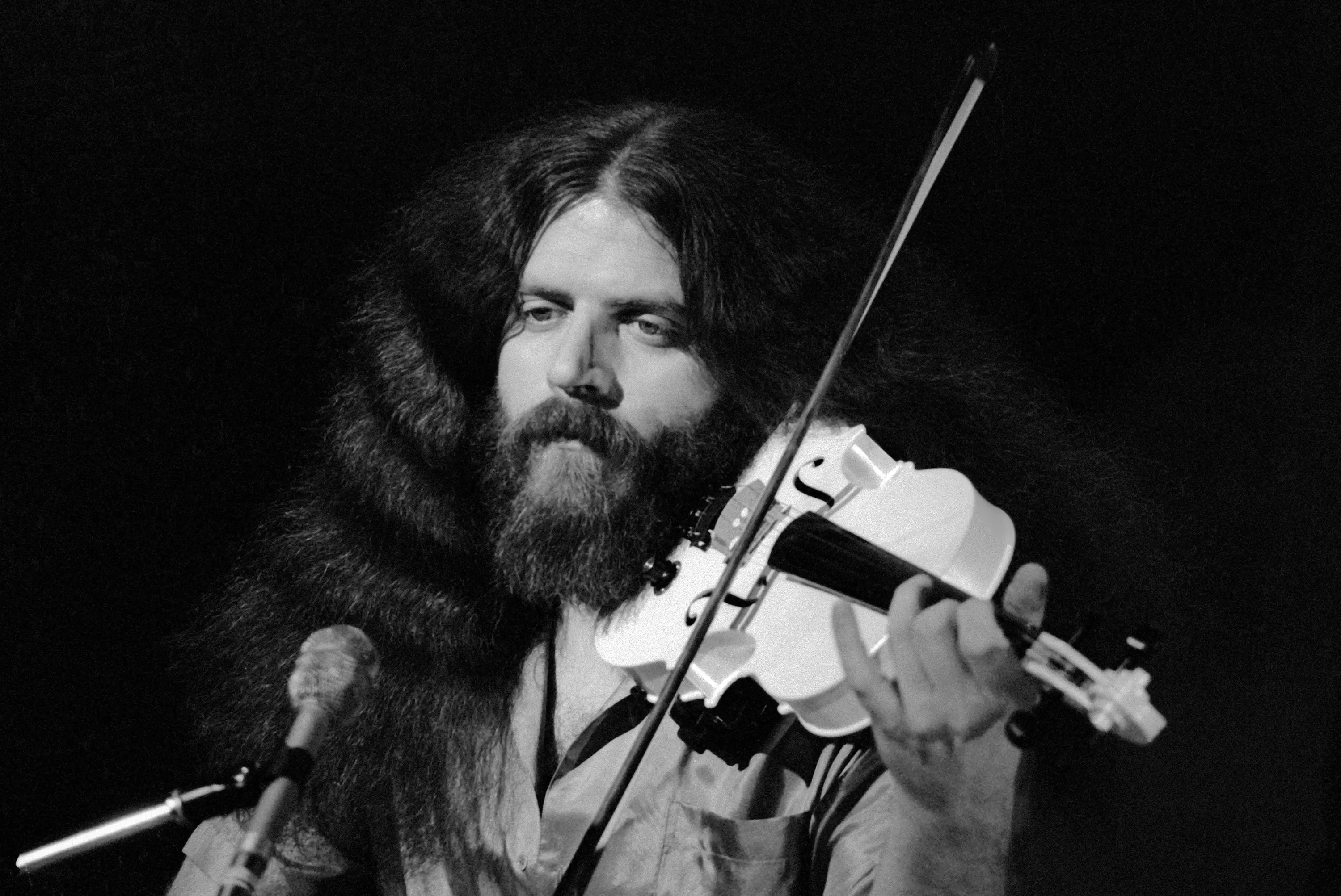 Robby Steinhardt plays a violin in front of a microphone.