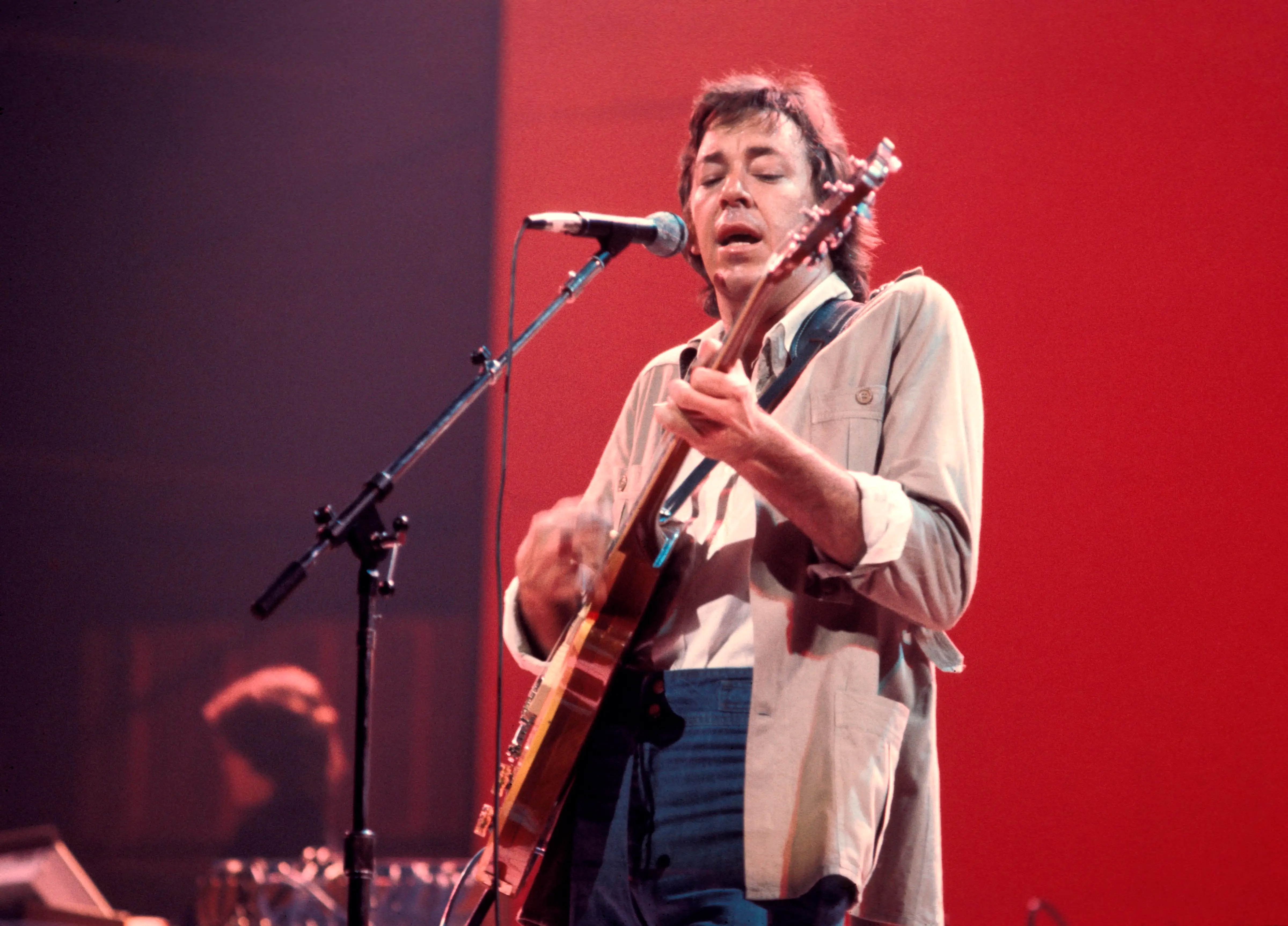 Boz Scaggs plays guitar and sings into a microphone on stage.