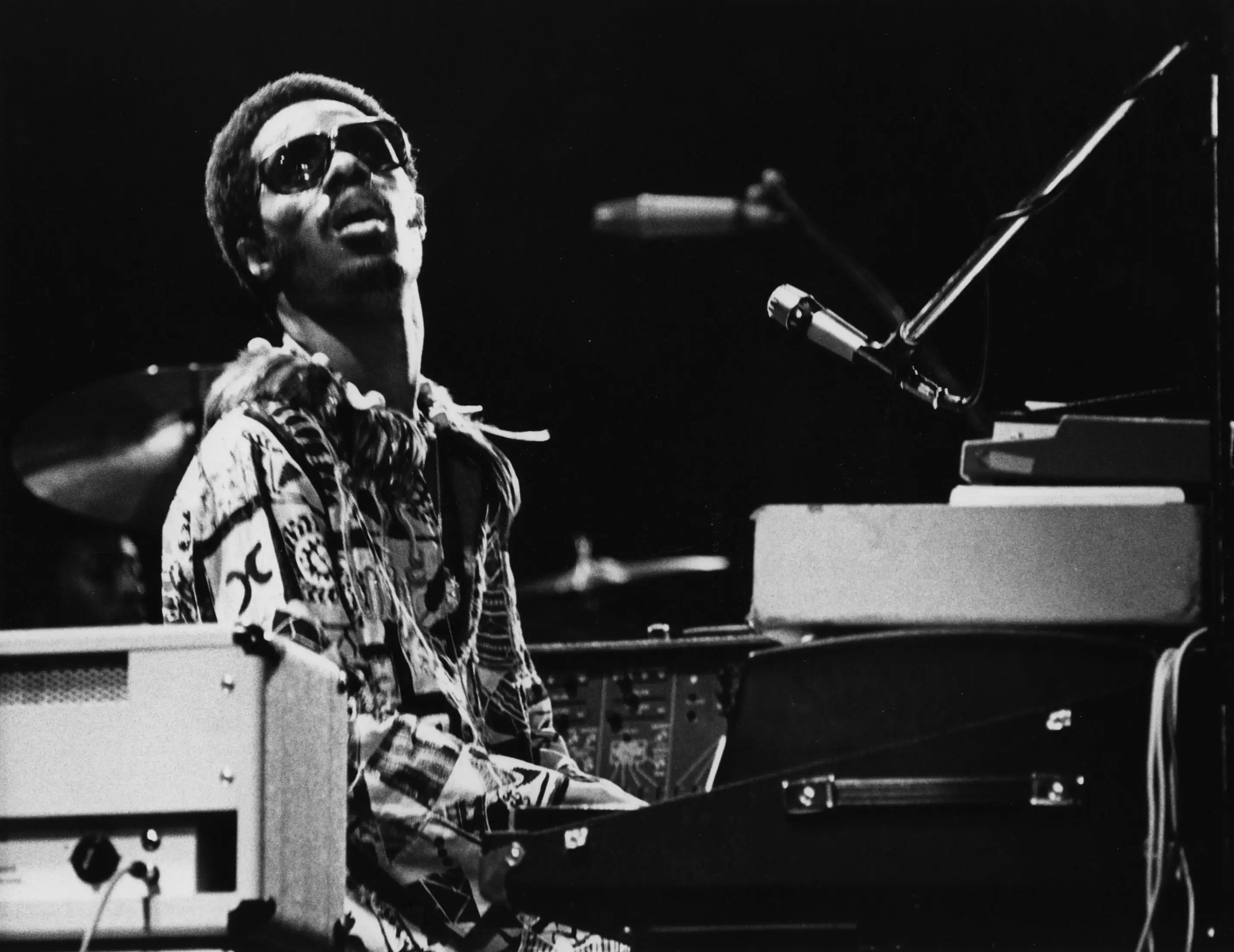 Stevie Wonder plays a piano and sings into a microphone on stage.
